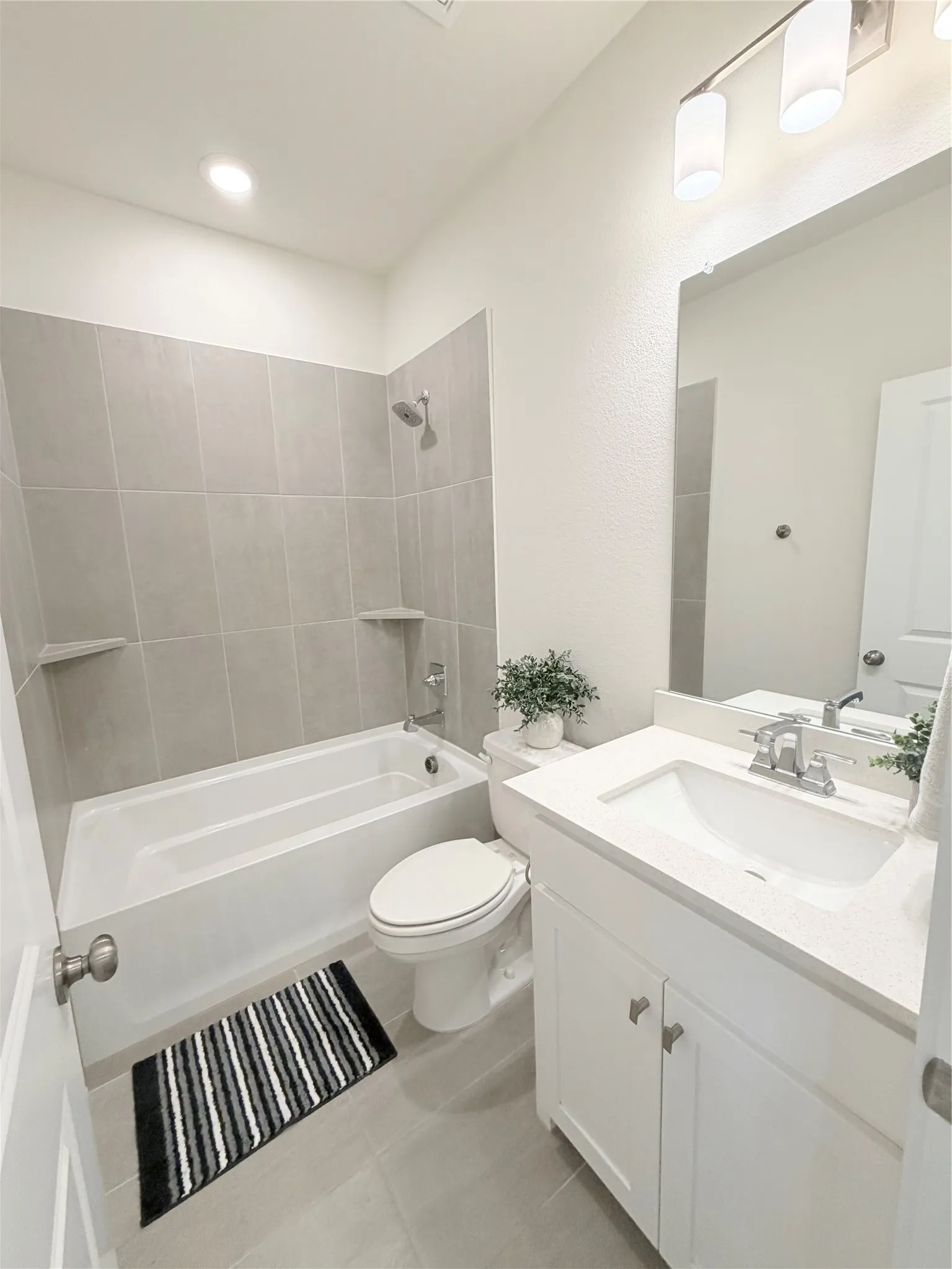 Bathroom featuring a white vanity with an undermount sink, a coordinating white toilet, and a bathtub with light gray tile surround