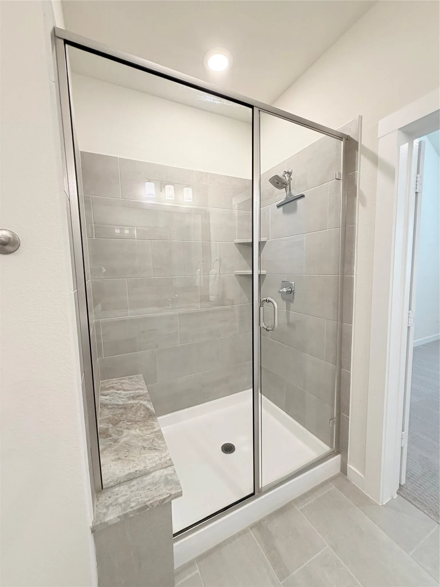 Glass-enclosed shower with a built-in bench, tiled walls, a rain showerhead, and recessed lighting