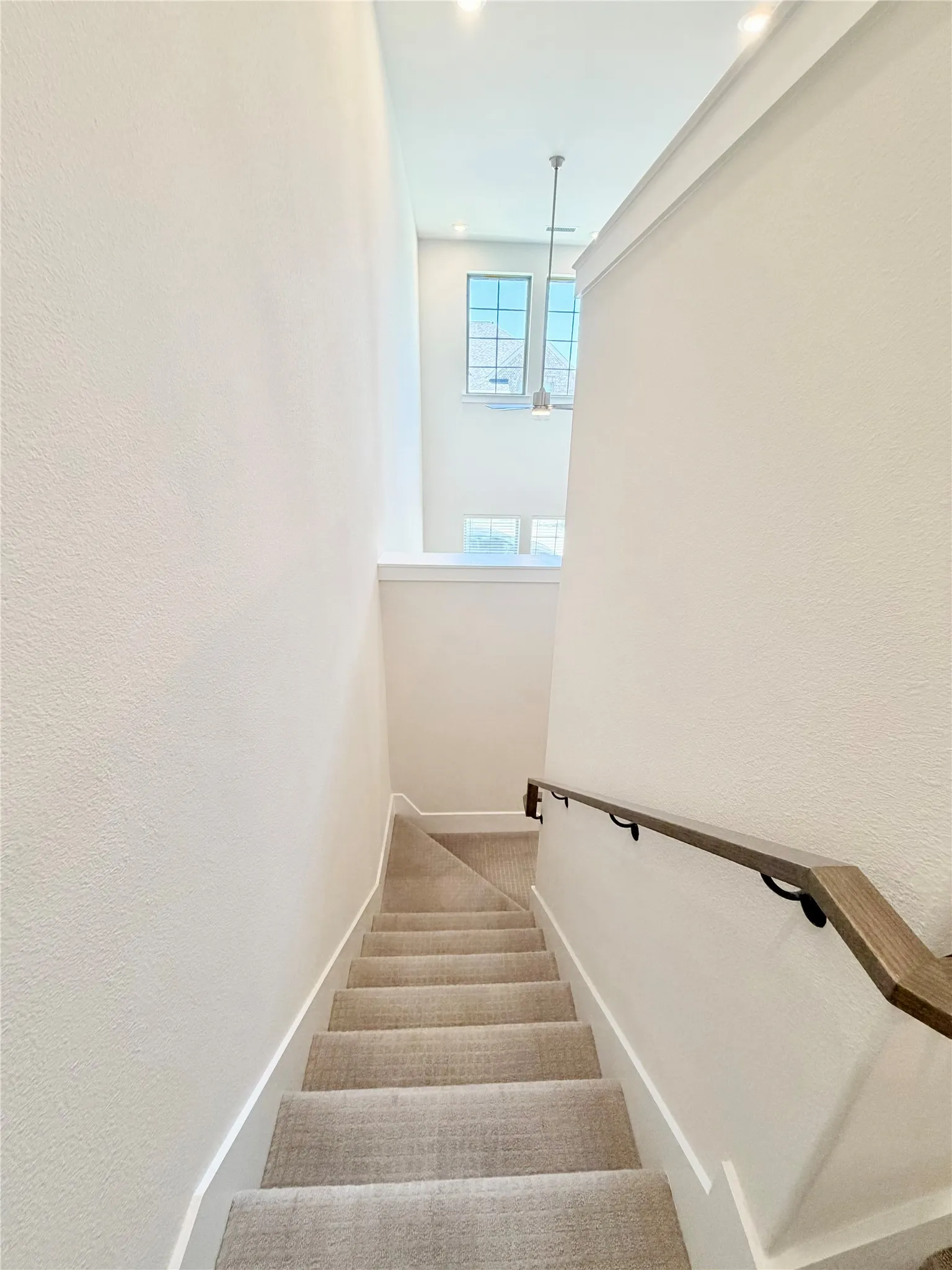 Carpeted staircase with wood handrail, recessed lighting, and high ceilings