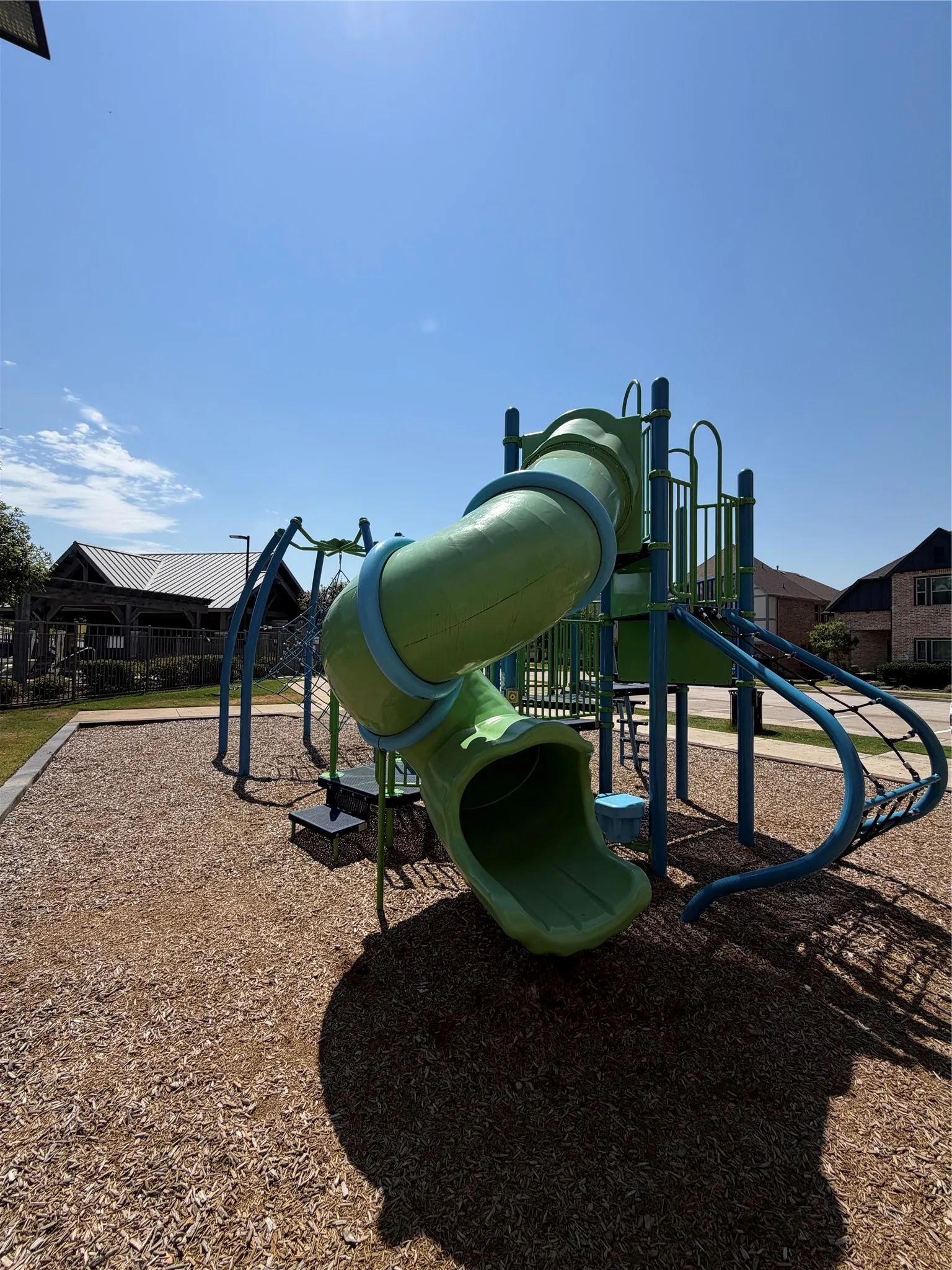Outdoor playground featuring a green enclosed slide, blue support beams, and a wood chip ground cover