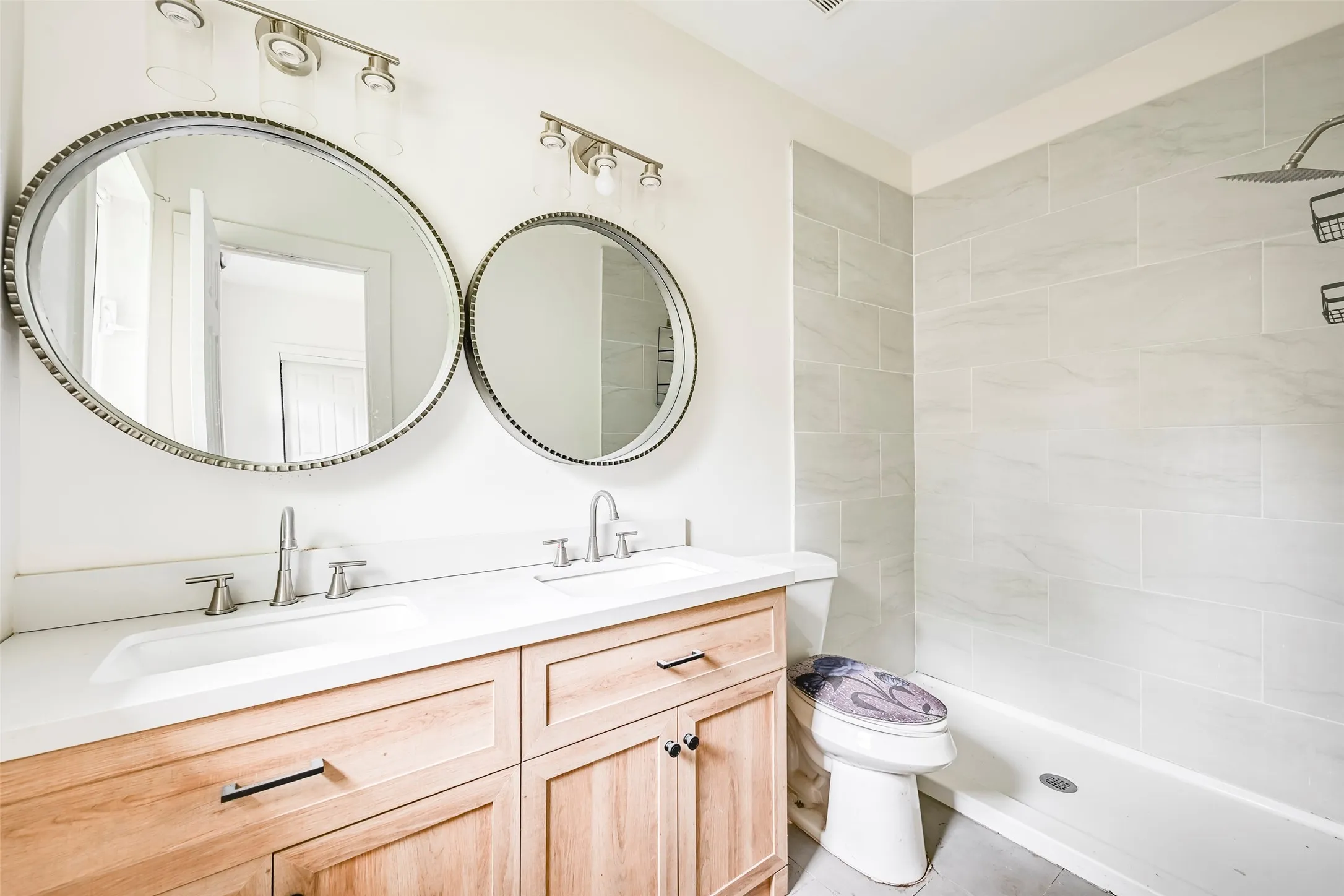 Dual vanity featuring light wood cabinetry, white countertops, and circular framed mirrors