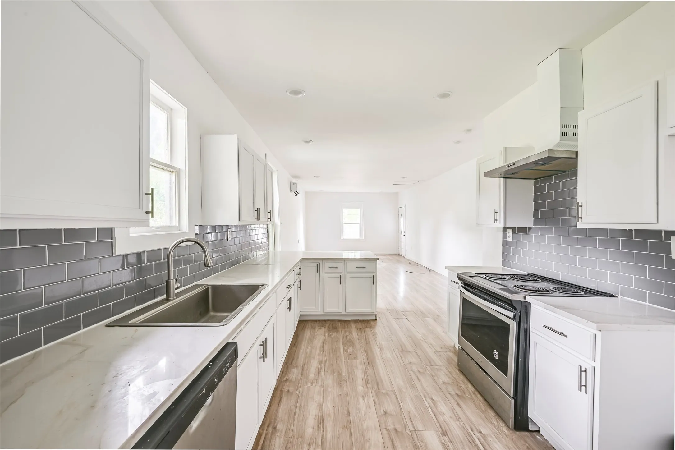 Modern kitchen featuring white cabinetry, light countertops, a stainless steel sink, a gray subway tile backsplash, and wood-finish flooring