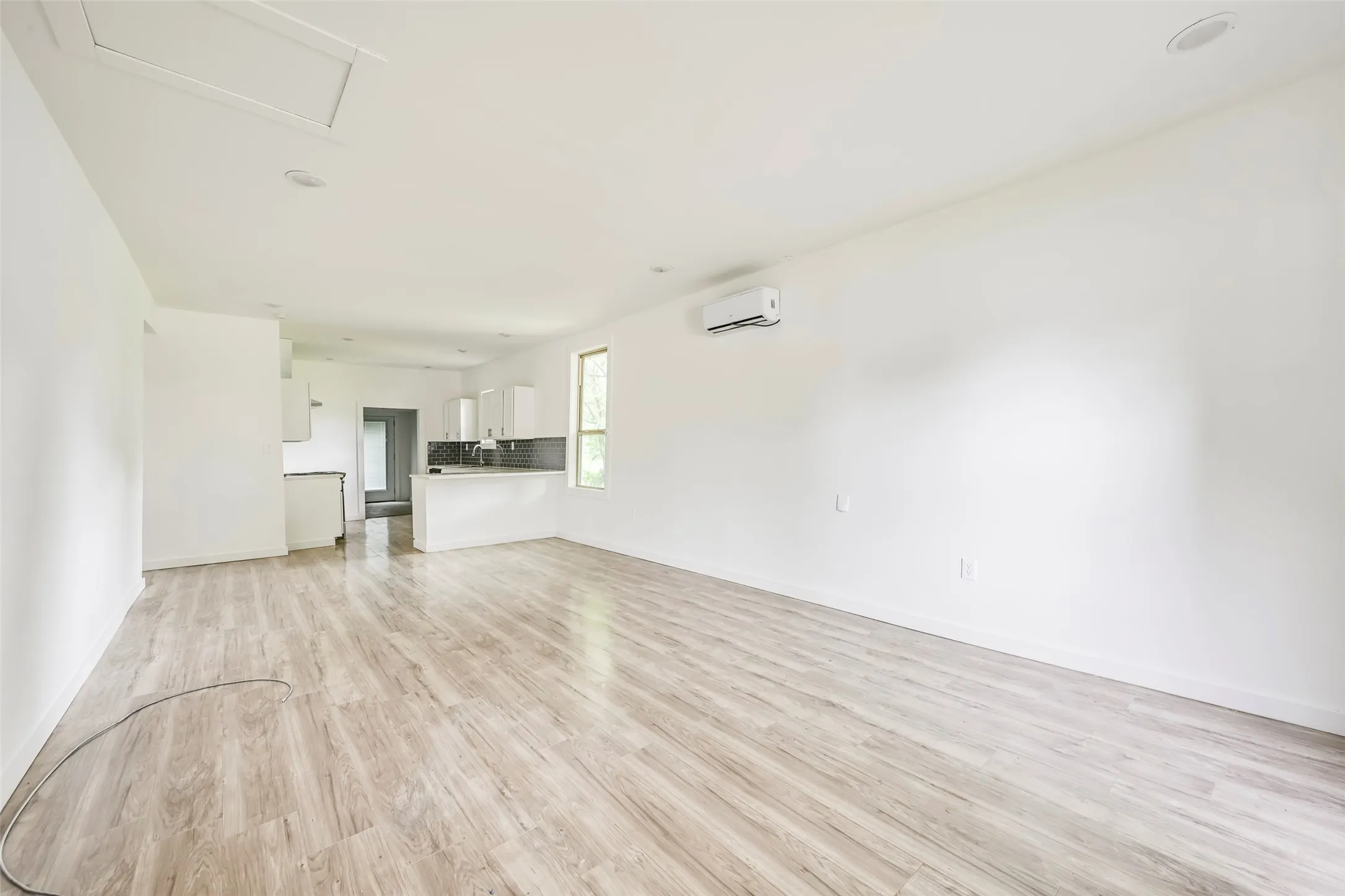 Open-concept living area featuring wood-finish flooring, recessed lighting, and a white wall-mounted mini-split system