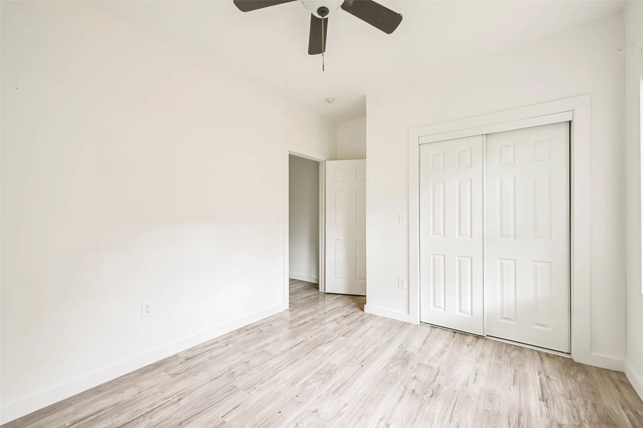 Room featuring wood-finish flooring, white walls, and a ceiling fan