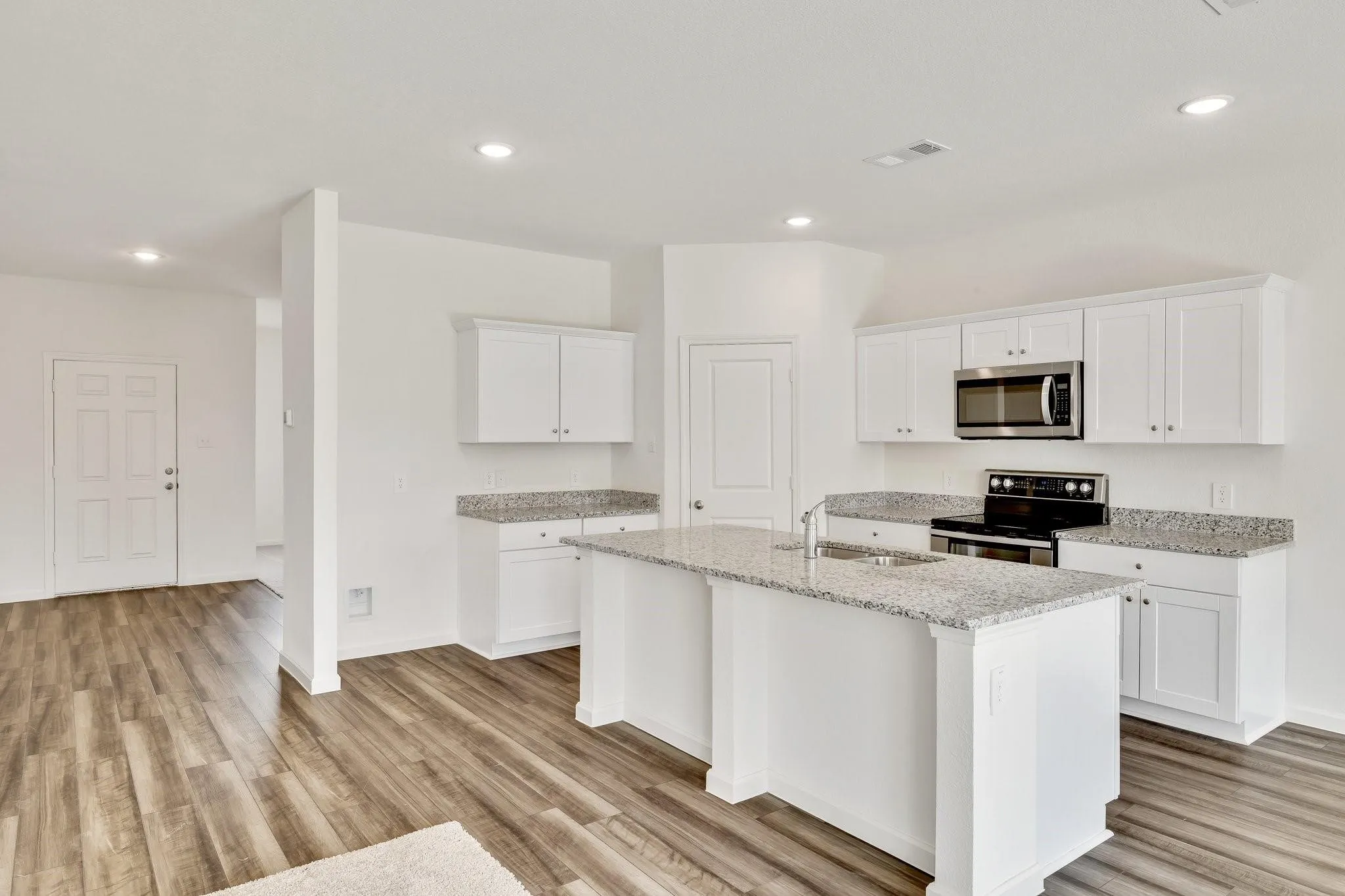 Kitchen featuring an island with a sink, white cabinetry, integrated stainless steel appliances, granite countertops, and wood-finish flooring