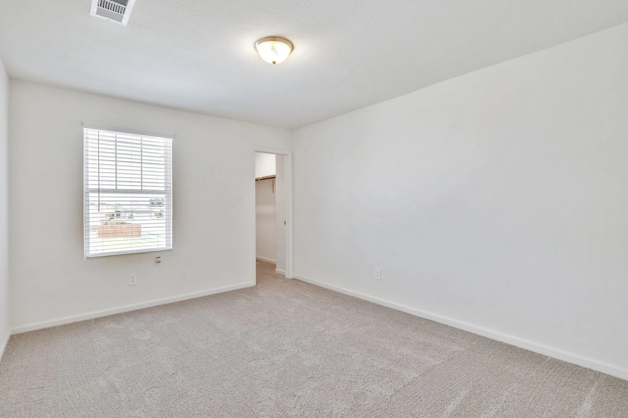 Carpeted room featuring a single window with blinds, a ceiling-mounted light fixture, and a visible closet entry
