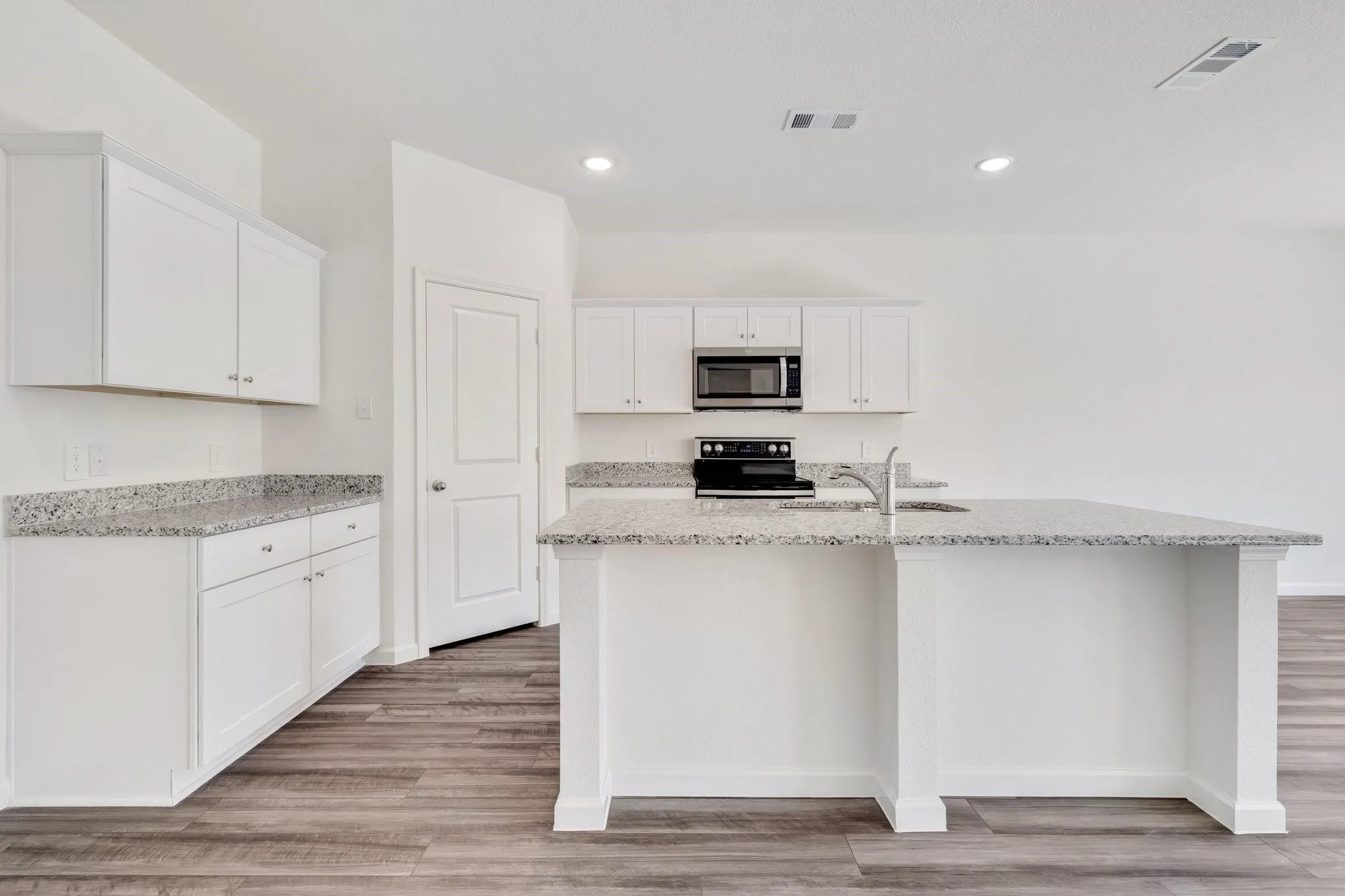 Kitchen featuring white cabinetry, speckled countertops, stainless steel appliances, a kitchen island with an integrated sink, and wood-finish flooring