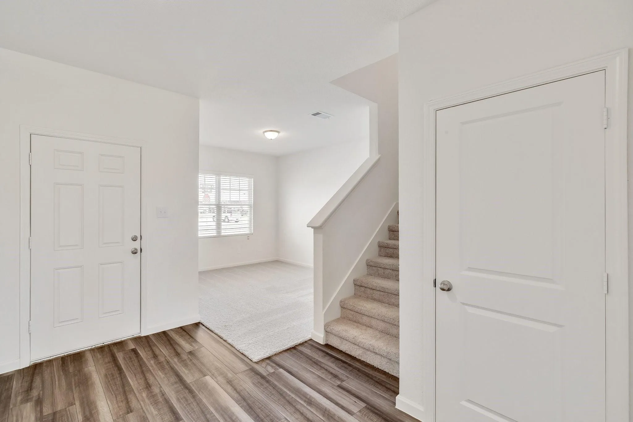 Entryway featuring wood-finish flooring, a white paneled door, and a staircase with carpeted treads