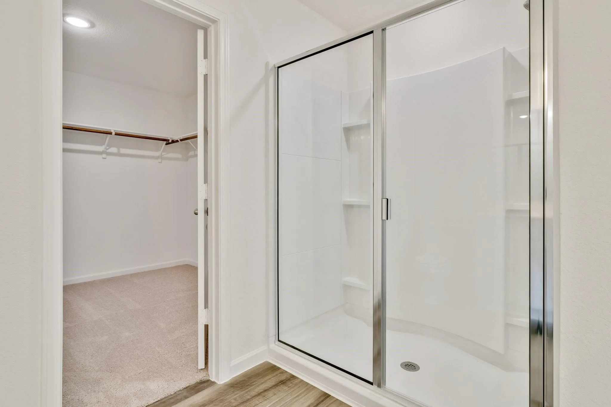 Glass-enclosed shower with white surround, integrated shelving, and a chrome-finish door frame