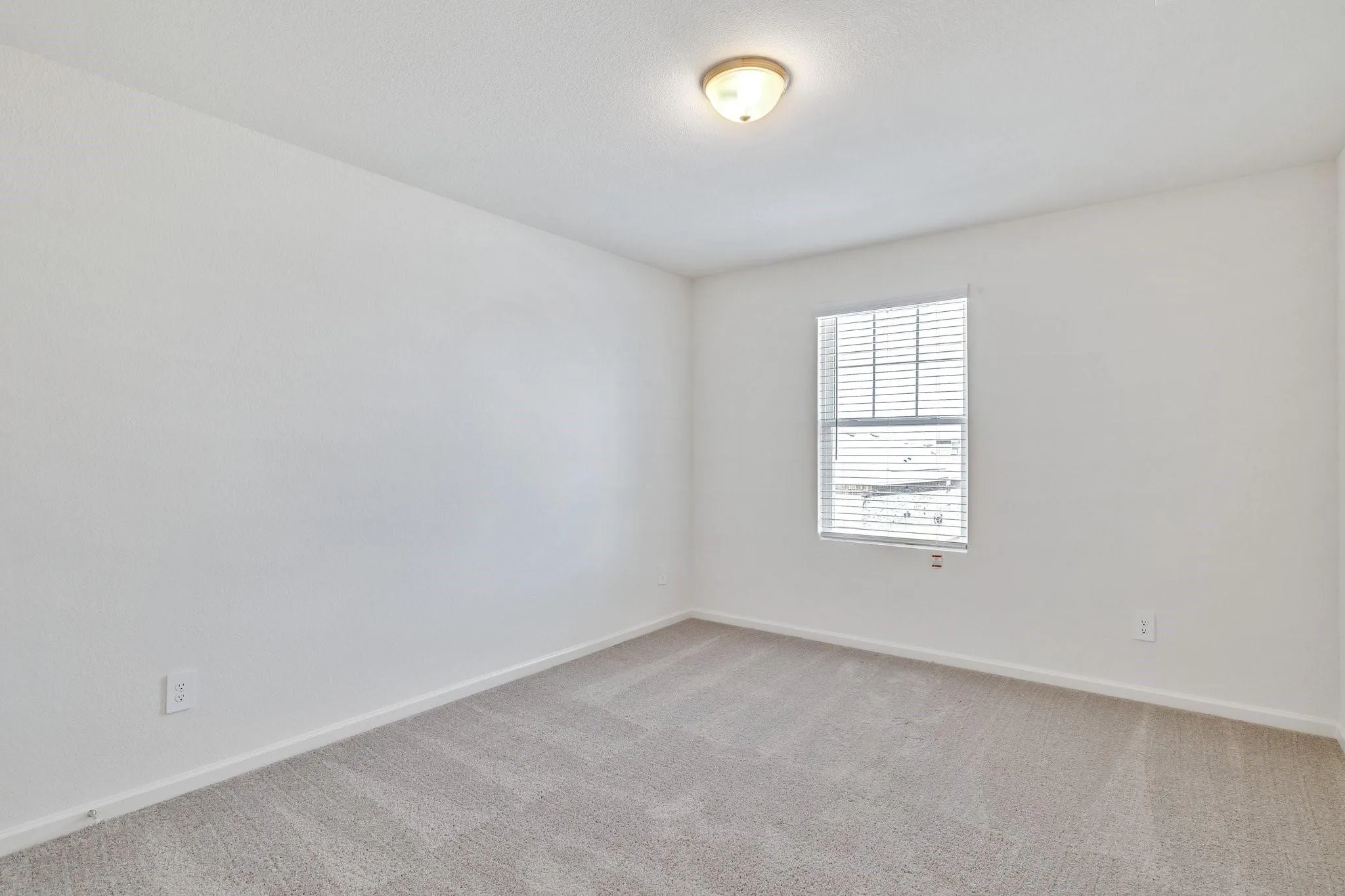 Bright room featuring light-colored carpet, white walls, and a single window with horizontal blinds