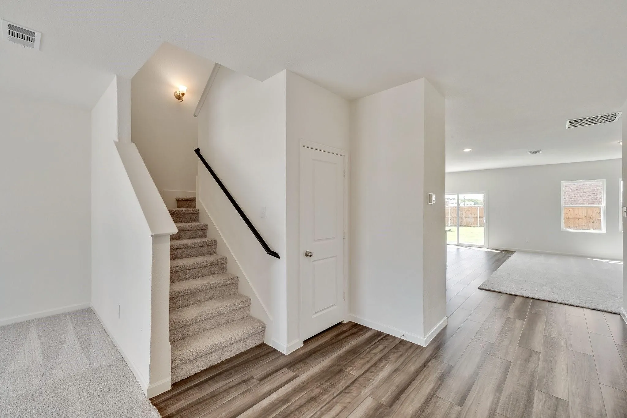 Carpeted staircase with a black handrail and sconce lighting