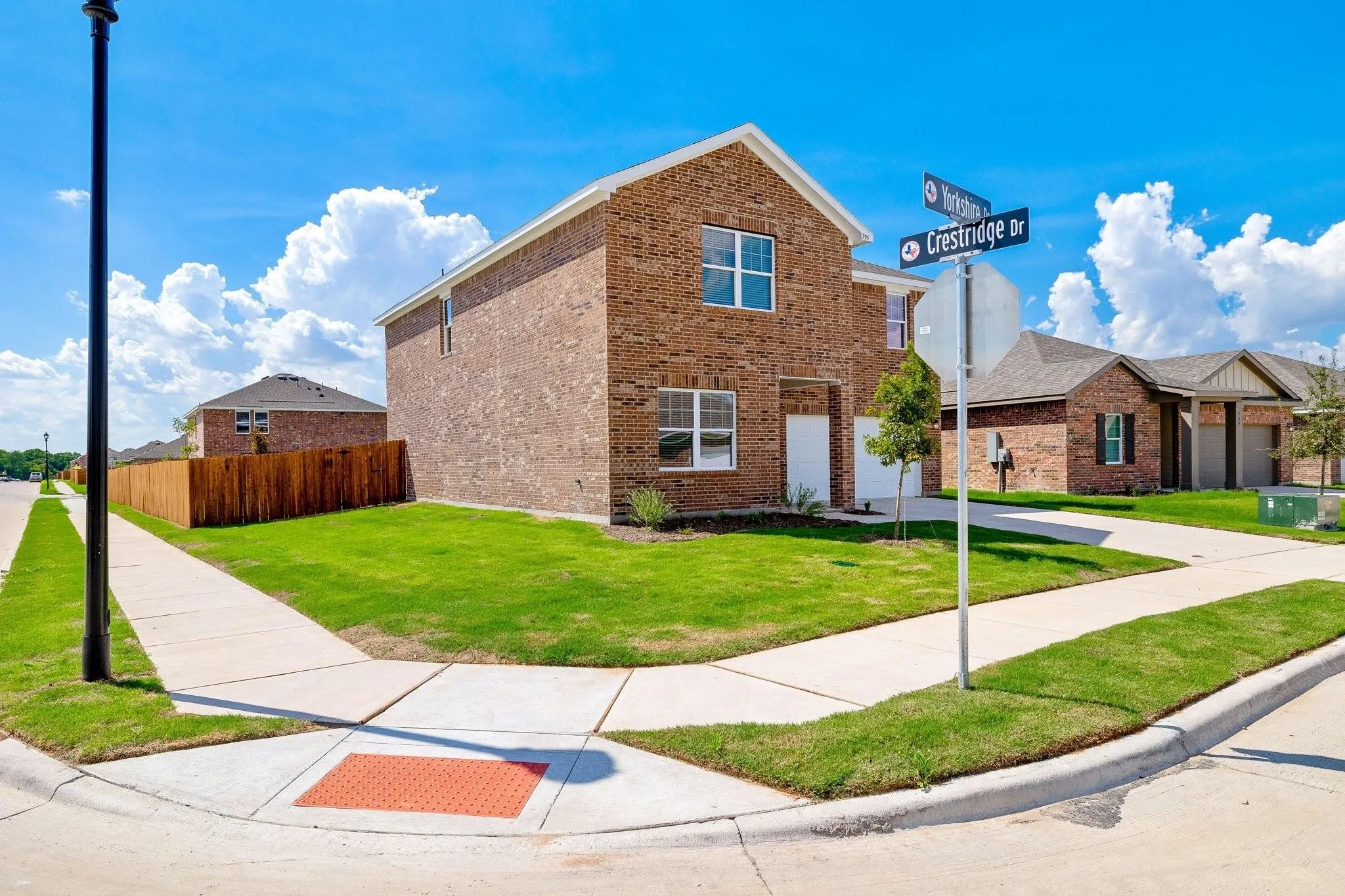 Brick exterior home situated on a corner lot, featuring a manicured lawn and privacy fence