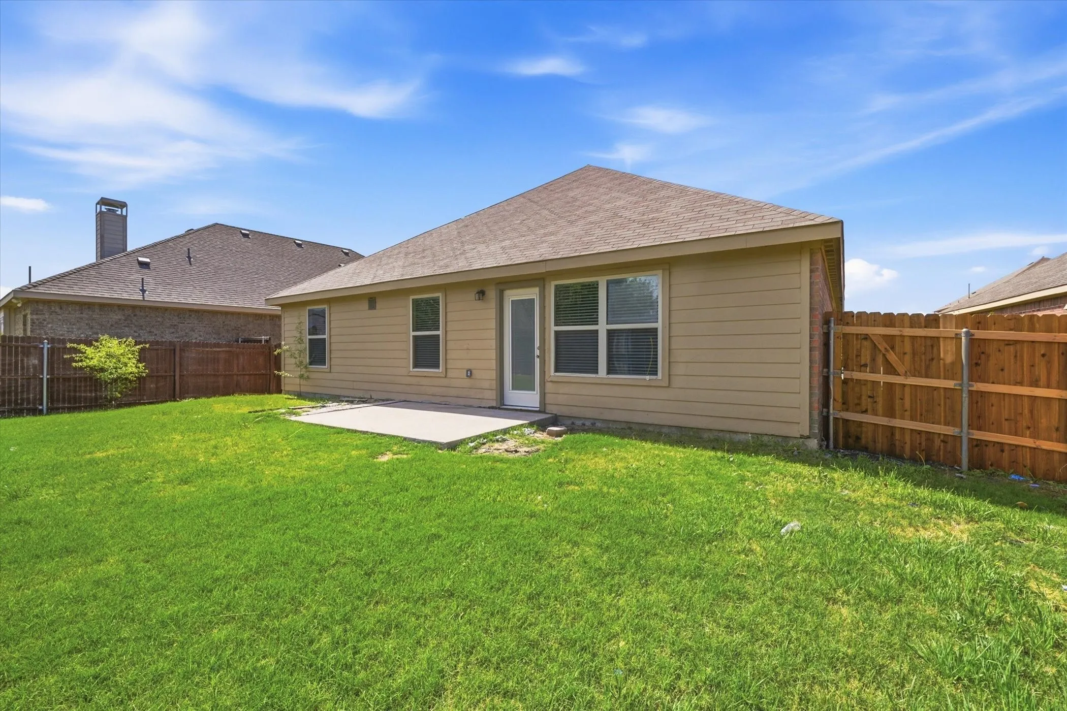 Spacious backyard featuring a concrete patio, wood fencing, and a tan siding exterior