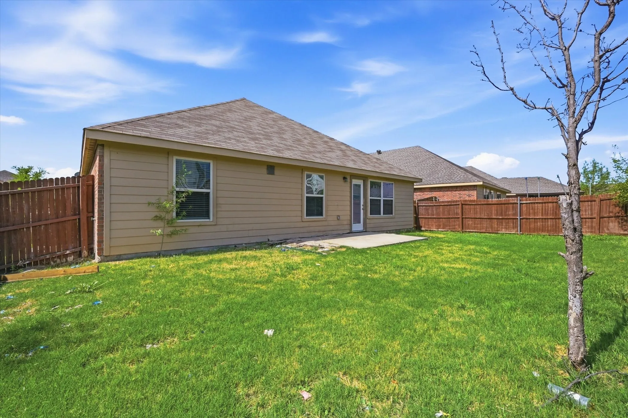 Expansive backyard featuring a manicured lawn, full privacy fencing, and a concrete patio