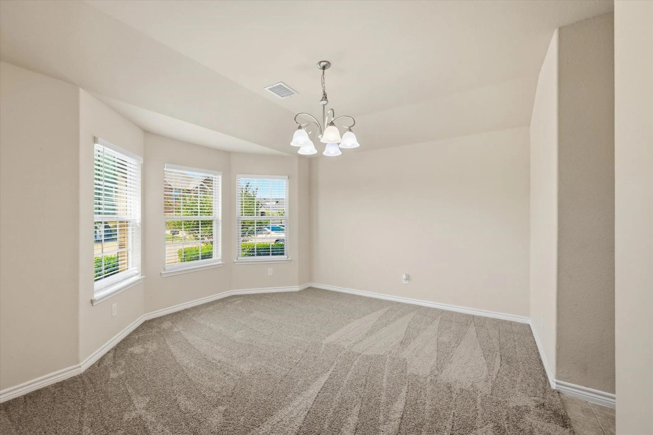 Bay window with three individual pane windows, neutral carpeting, vaulted ceiling, and overhead chandelier fixture