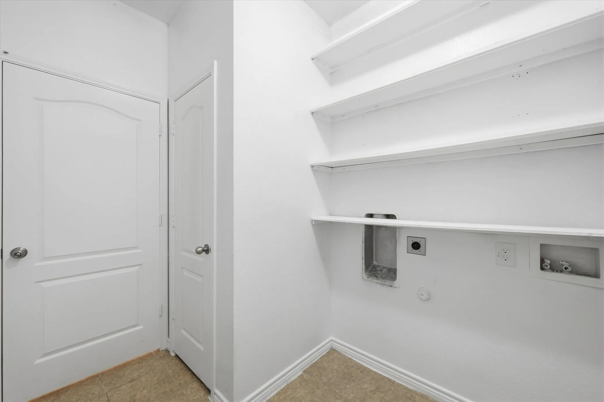 Dedicated laundry area featuring a tiled floor, multiple white storage shelves, and utility hookups