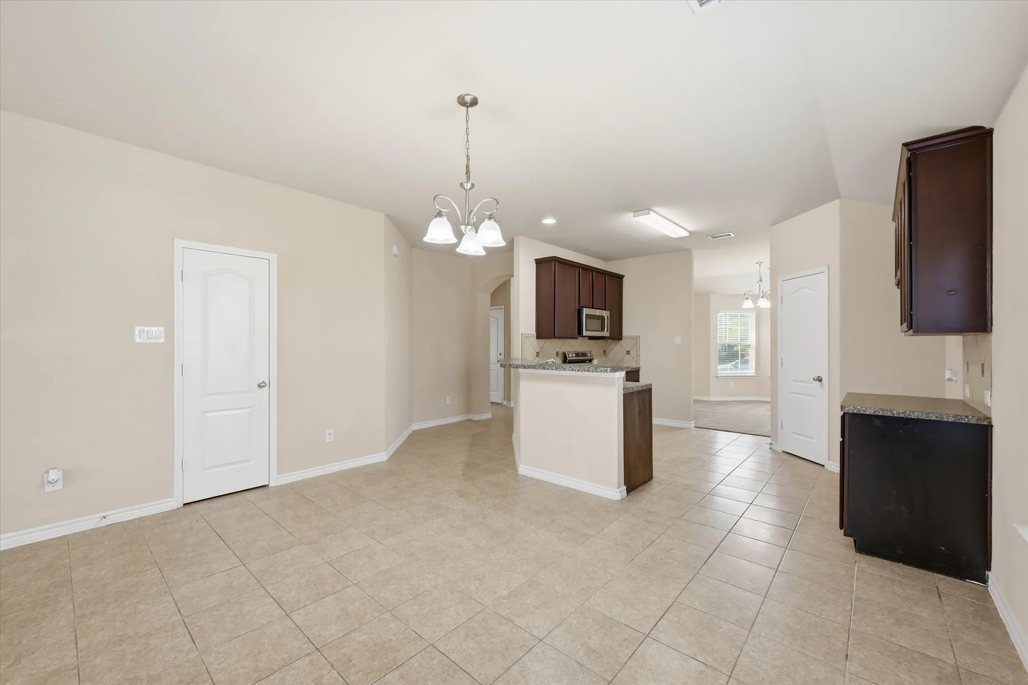 Open-concept living space with tile flooring throughout, featuring a kitchen peninsula with a breakfast bar, dark wood-finish cabinetry, and recessed lighting