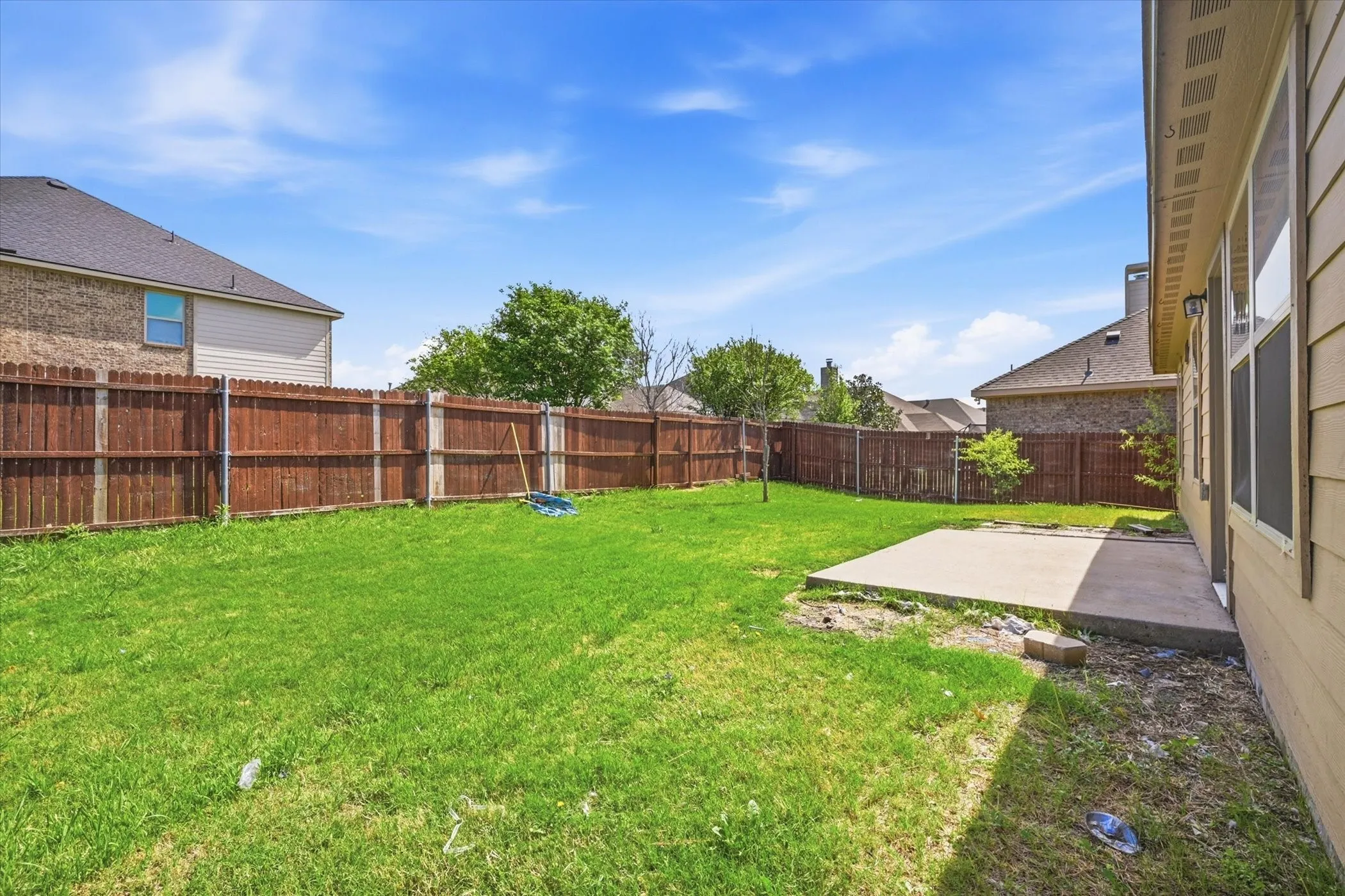 Expansive backyard featuring a manicured lawn, a full wood privacy fence, and a concrete patio slab