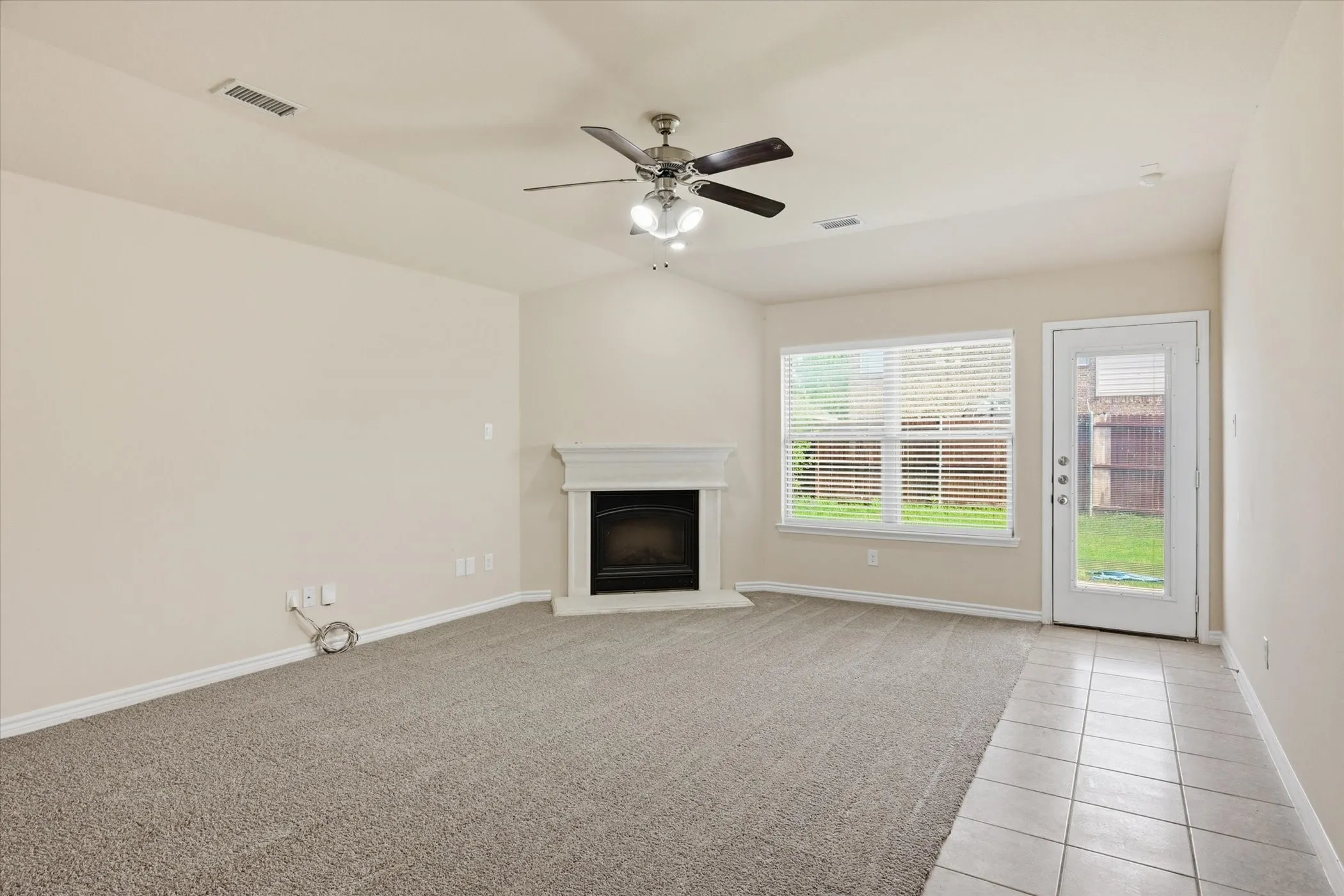 Living area featuring a fireplace with a white mantel, ceiling fan with integrated lighting, and carpet flooring