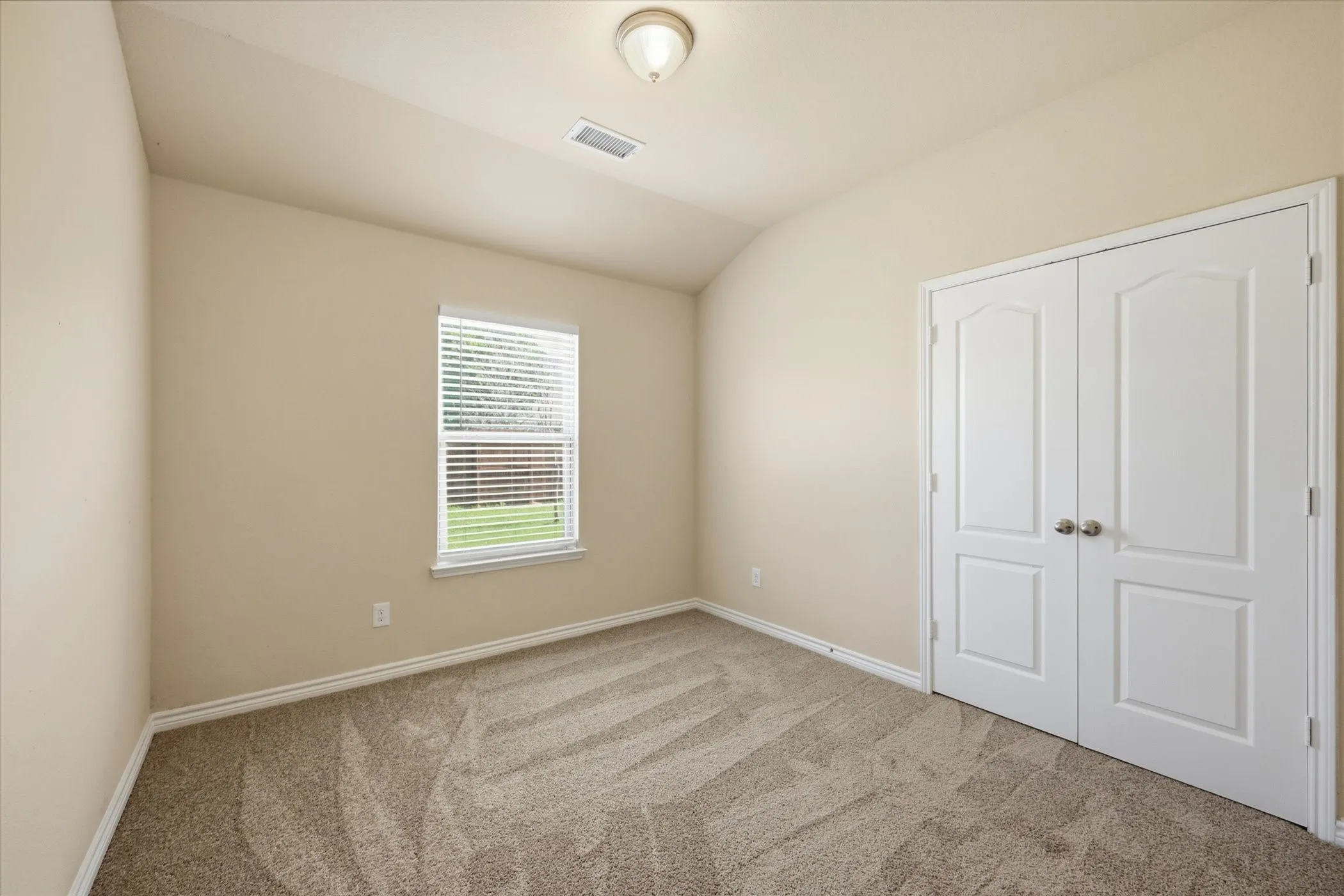 Room featuring neutral wall tones, textured carpet flooring, a window with horizontal blinds, white trim, and white bi-fold closet doors