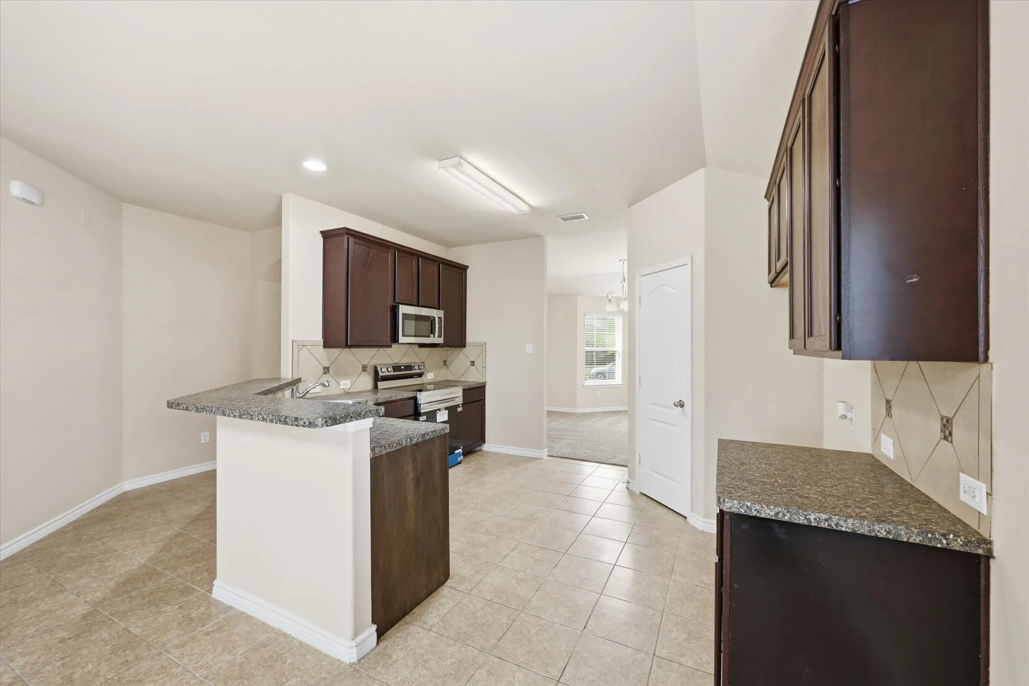 Kitchen featuring dark wood-finish cabinetry, speckled countertops, tile flooring, and a tile backsplash with decorative accents