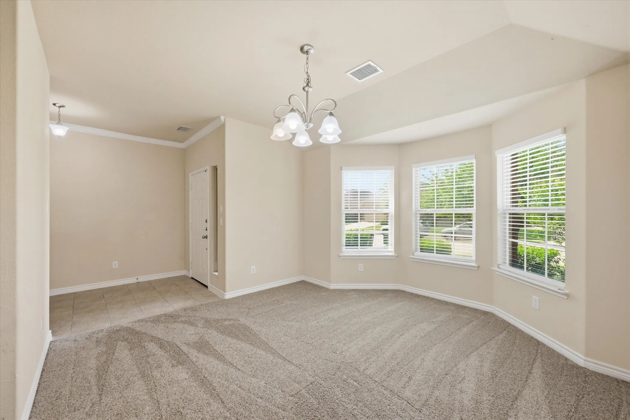 Bright interior space featuring a multi-window bay, neutral-toned walls, crown molding, and a decorative chandelier