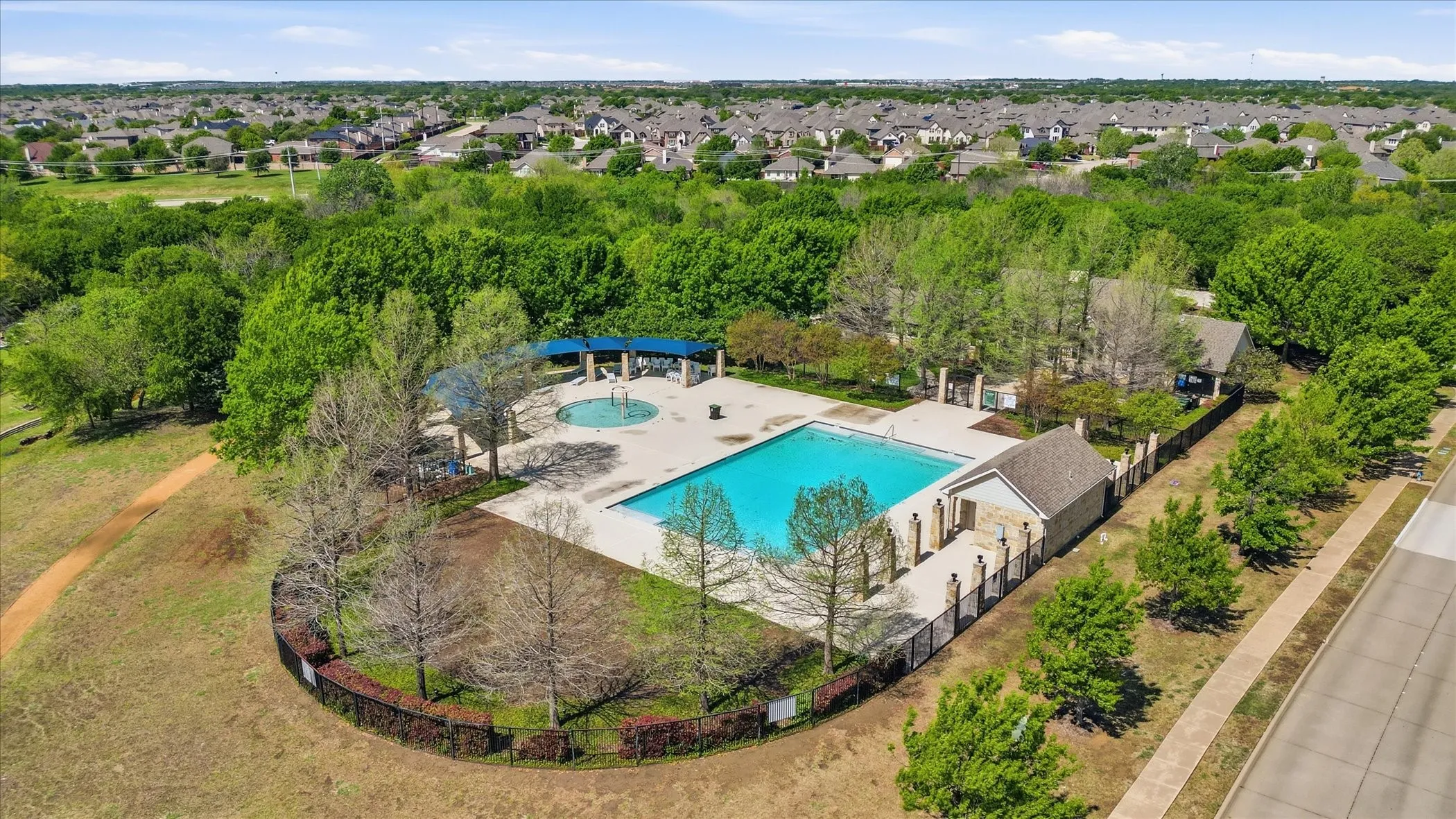 Community pool area featuring a large swimming pool, circular splash pad, and surrounding fenced patio
