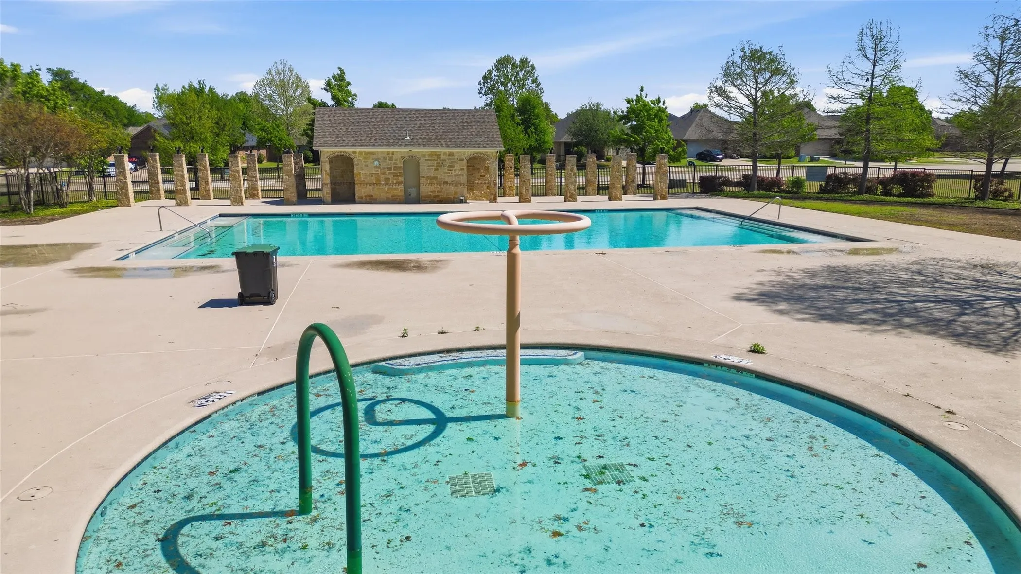 Expansive outdoor swimming pool area featuring a large main pool, a circular wading pool with a water feature, and a stone-clad building