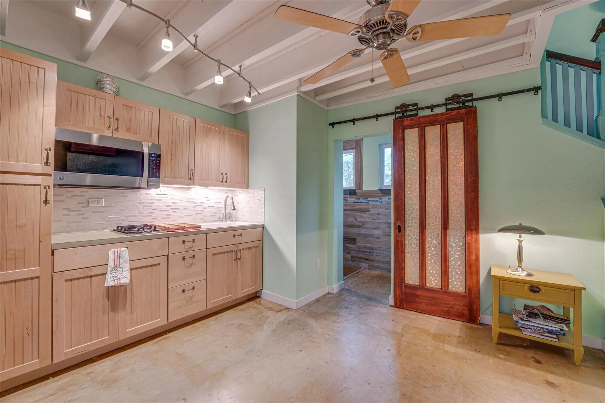 Compact kitchen featuring light wood cabinetry, white subway tile backsplash, and a stainless steel microwave