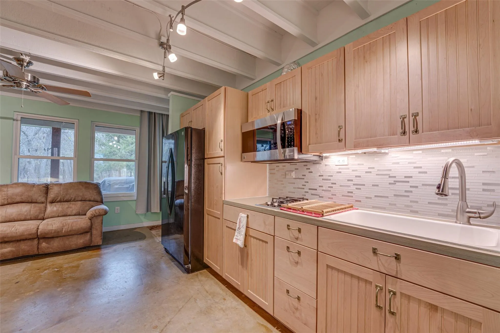 Kitchenette featuring light wood-finish cabinetry, a stainless steel microwave, and a black refrigerator