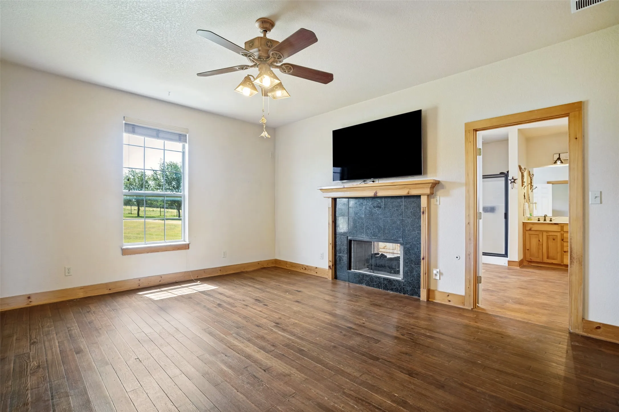 Spacious room featuring wood-finish flooring, a built-in fireplace with a dark stone surround, and a ceiling fan with integrated lighting
