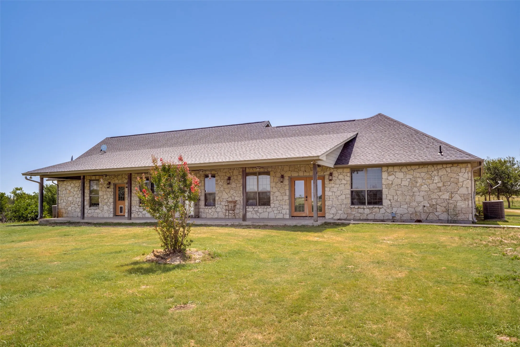 Stone exterior residence featuring a covered porch, multiple large windows, and a dark shingle roof