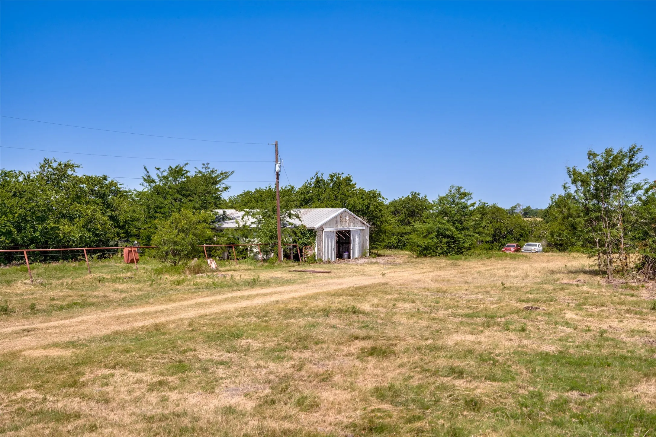 Expansive outdoor space featuring a dirt track and a metal outbuilding with an open doorway