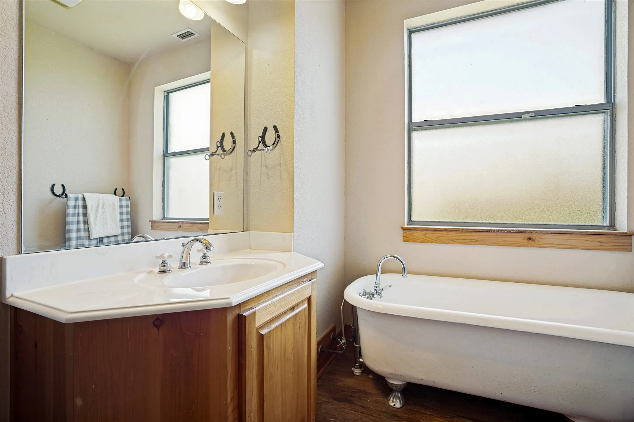 Bathroom featuring a clawfoot tub, wood-finish flooring, a single-basin vanity with an integrated sink, a large mirror, and a frosted window