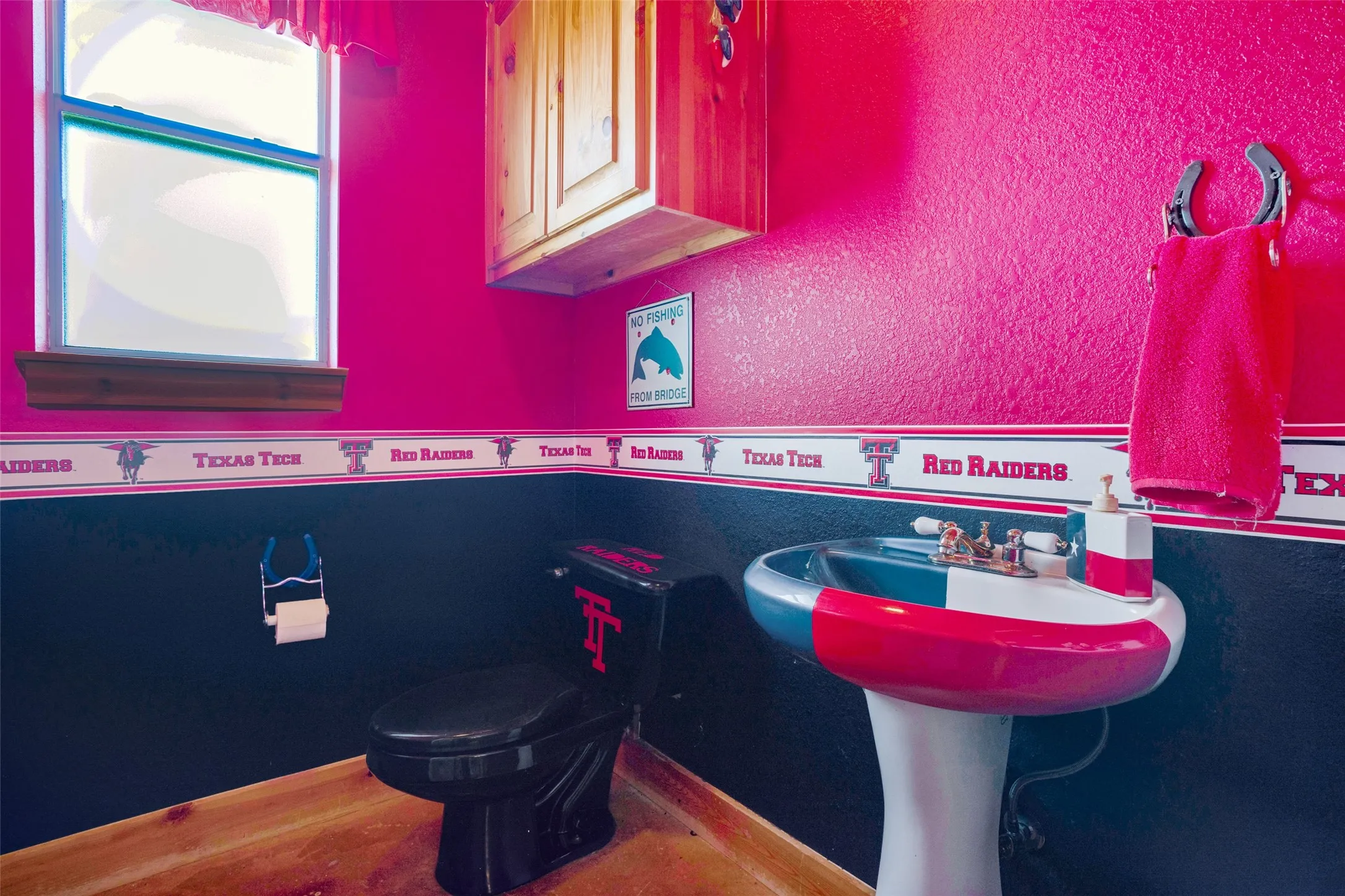 Pedestal sink with brass-finish dual-handle faucet, black toilet, wood-finish flooring, and a single window