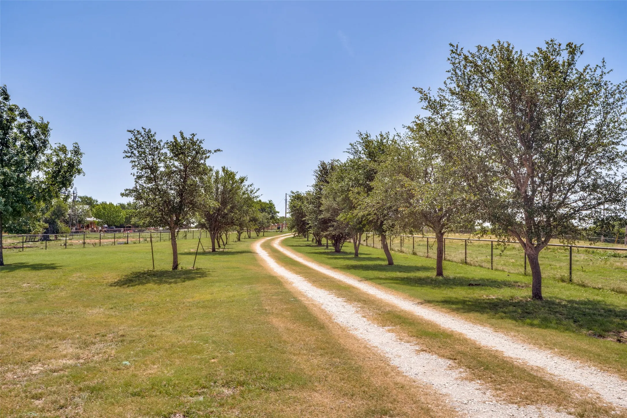Gravel driveway bordered by mature trees and expansive grassed areas
