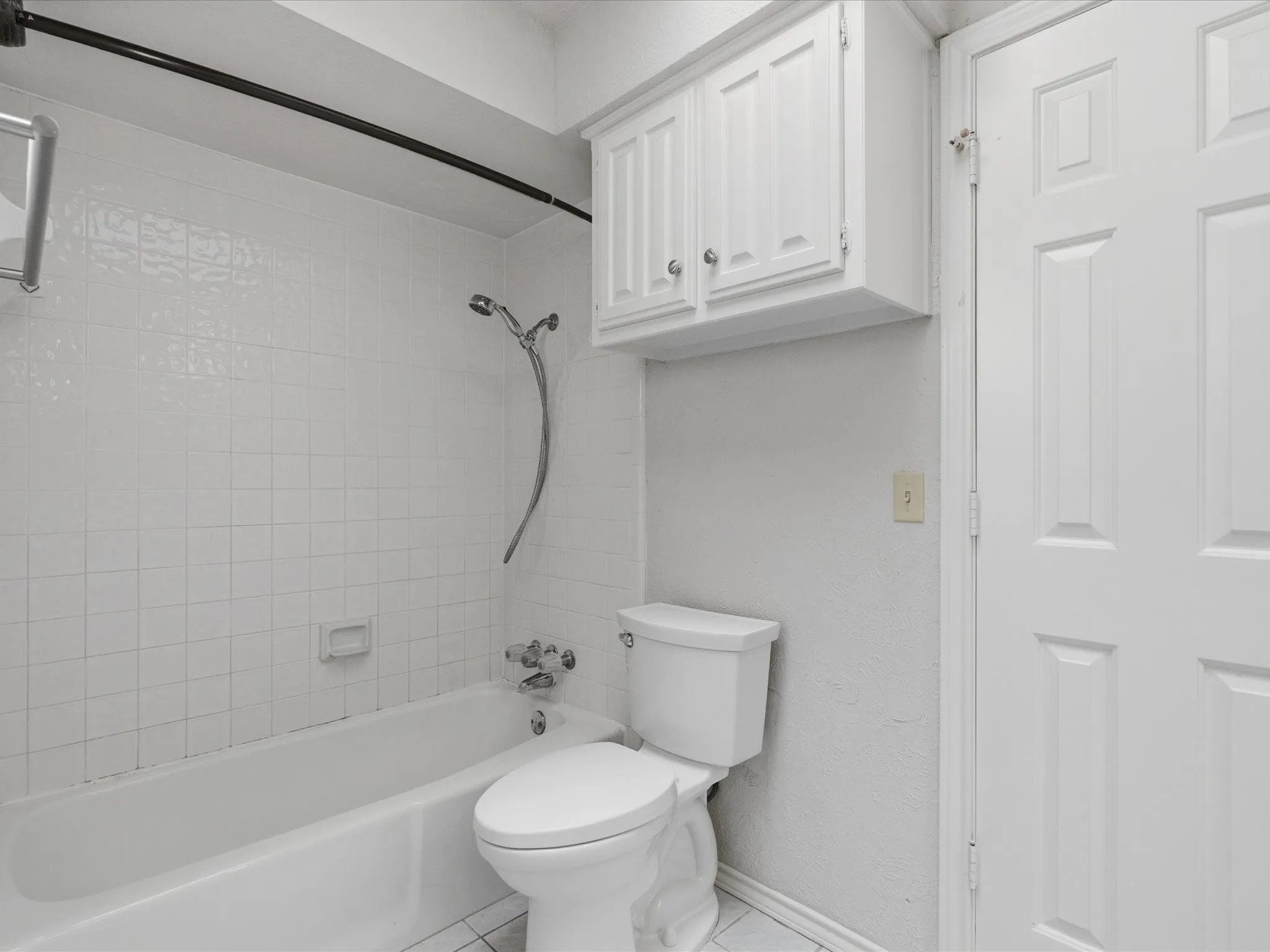 White tiled bath and shower combination with a wall-mounted shower head, chrome fixtures, and a white paneled door