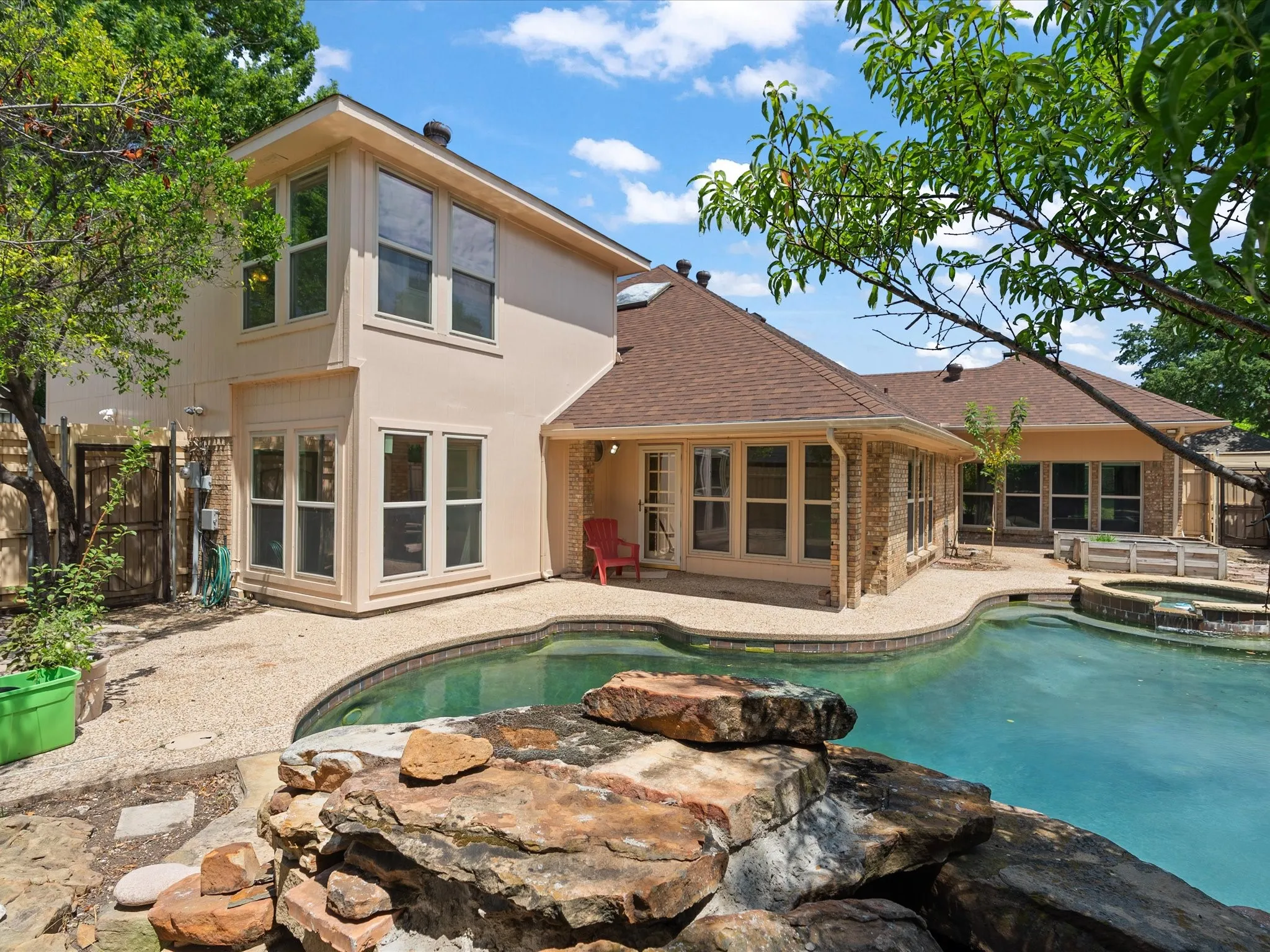Stucco exterior with multiple large windows, a shingle roof, and a curved swimming pool with integrated spa and rock waterfall feature