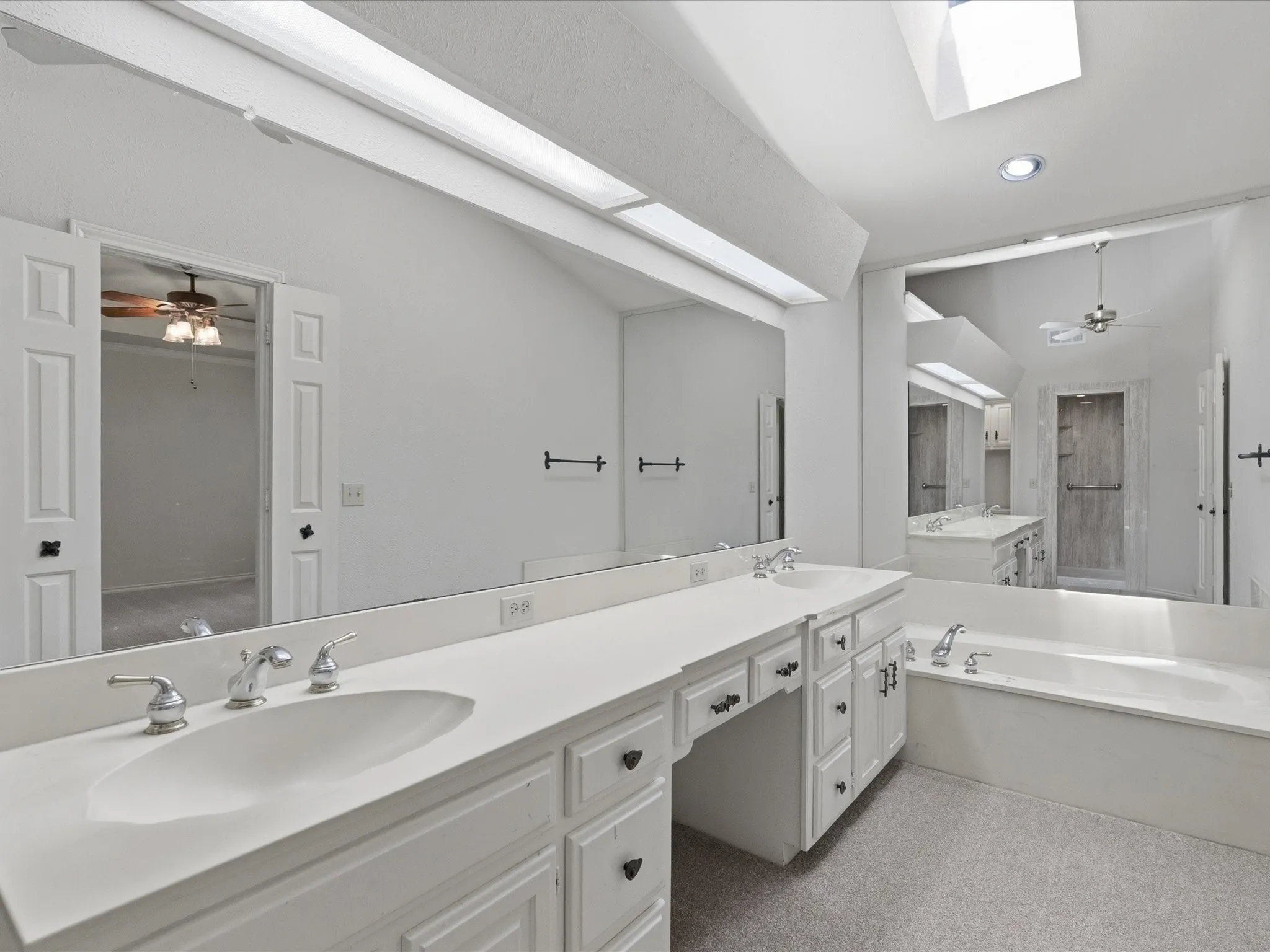 Bright bathroom with a vaulted ceiling, dual skylights, and a built-in vanity featuring two integrated sinks with chrome fixtures