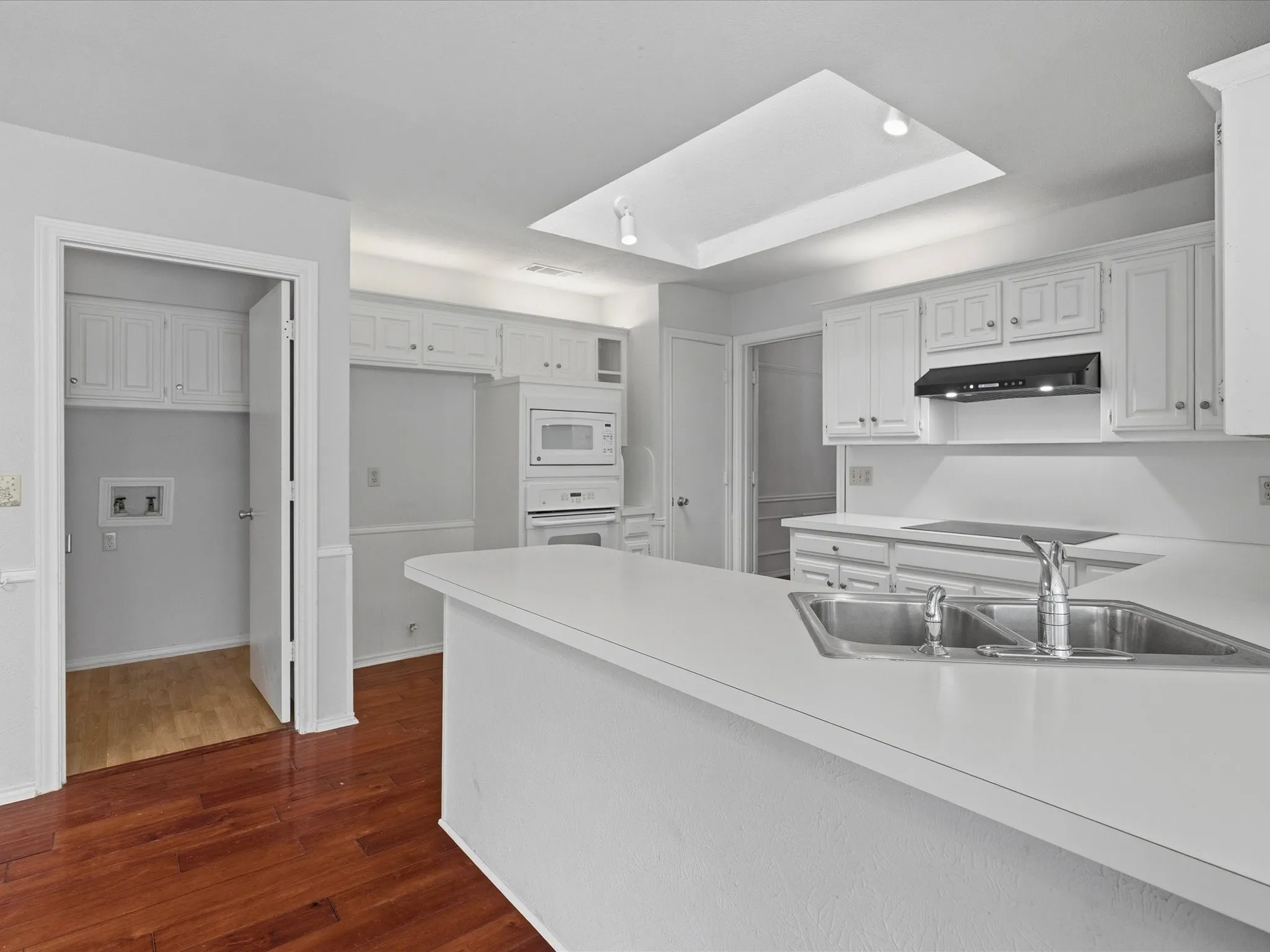 Kitchen featuring a double basin stainless steel sink with chrome faucet, white countertops, built-in white appliances, and a skylight