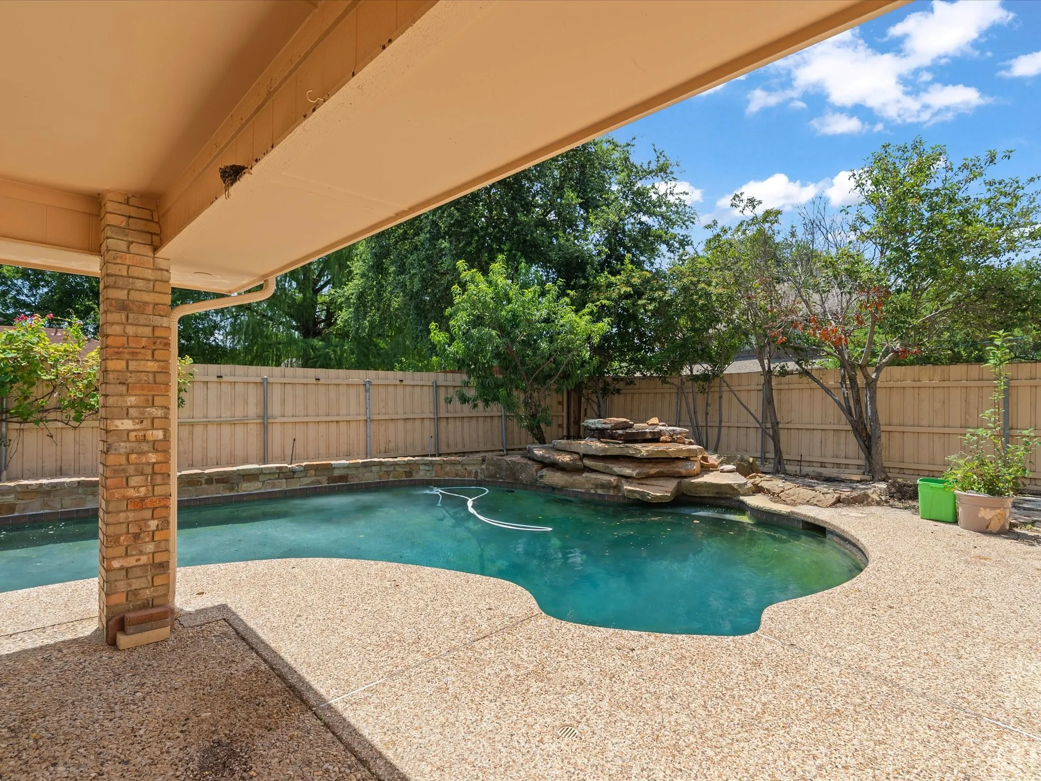 Covered patio with a brick column, exposed aggregate patio, and an in-ground pool featuring a rock waterfall