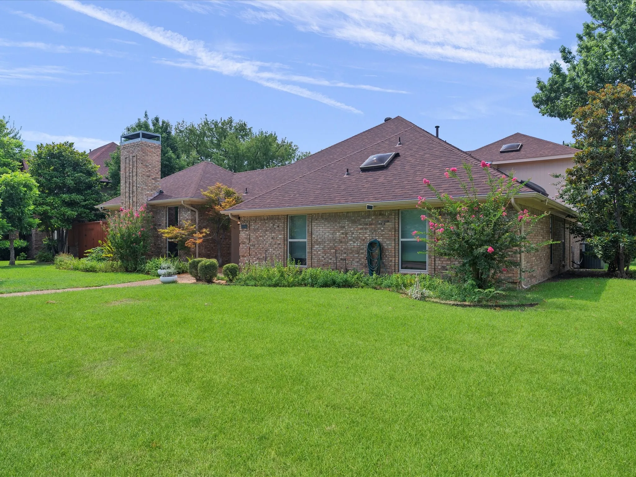 Brick exterior featuring a brown shingle roof, tall brick chimney, and multiple skylights