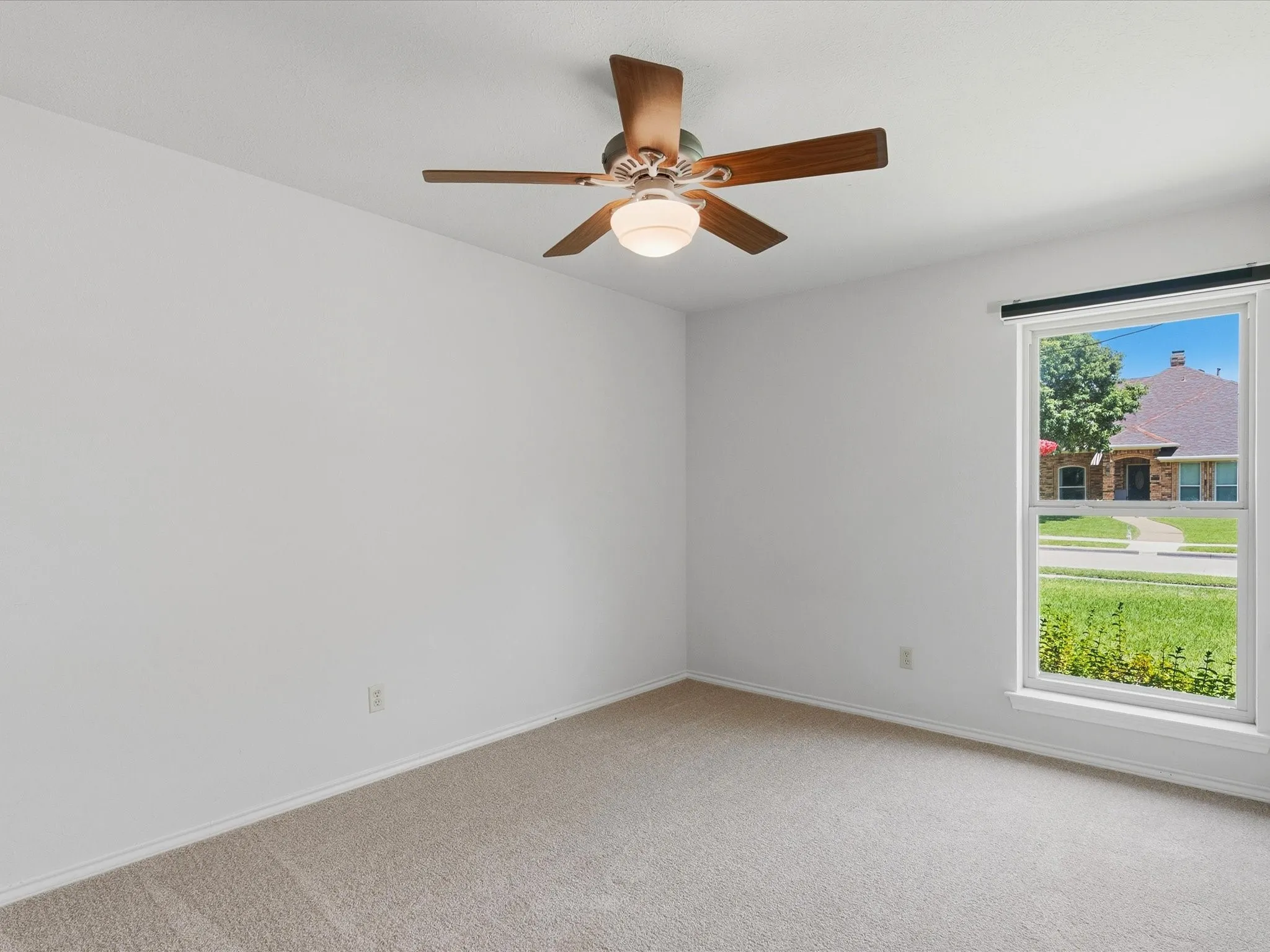 Carpeted interior room featuring a ceiling fan with light fixture, neutral wall paint, and a window with white trim