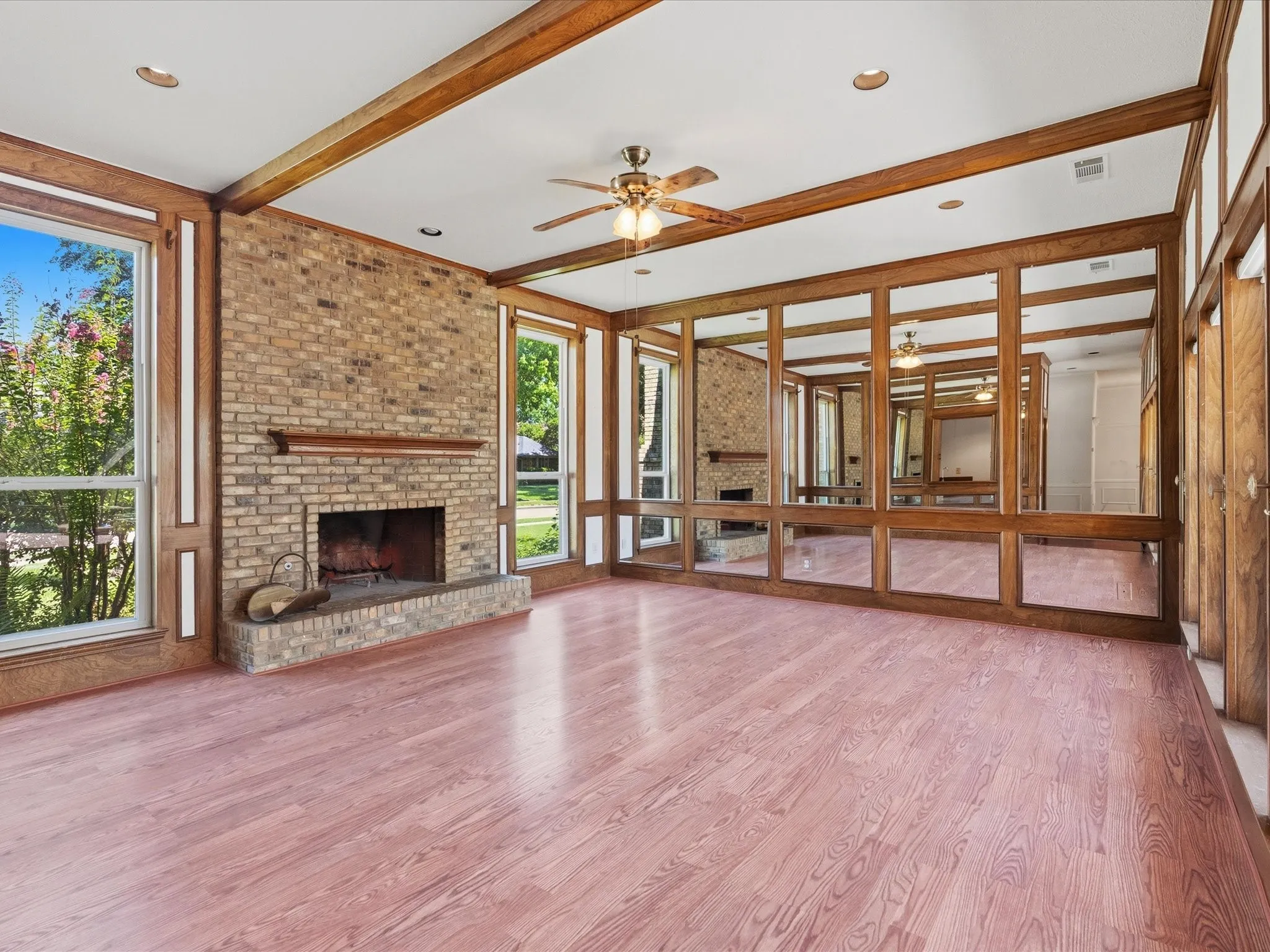 Spacious room featuring wood-finish flooring, a brick fireplace with a wood mantle, and exposed wood beams on the ceiling