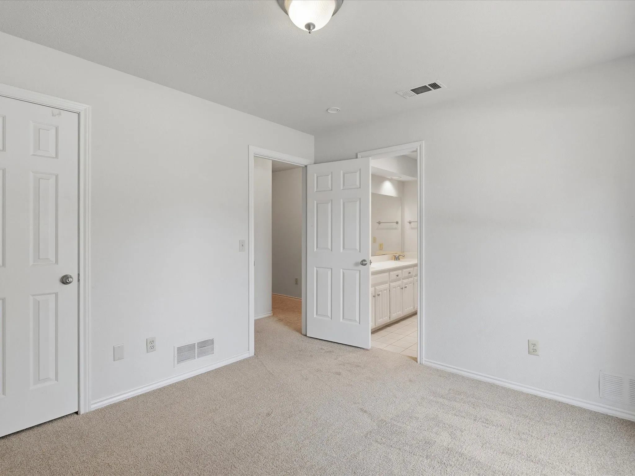 Carpeted interior room with white walls, two white panel doors, and overhead lighting