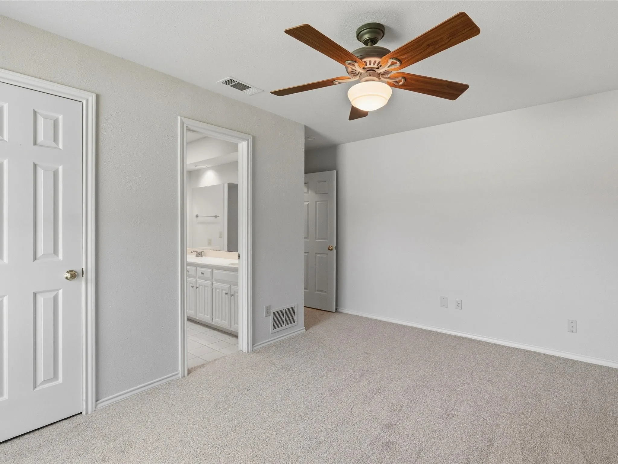Neutral-toned carpeted room with a ceiling fan featuring wood-finish blades and an integrated light fixture