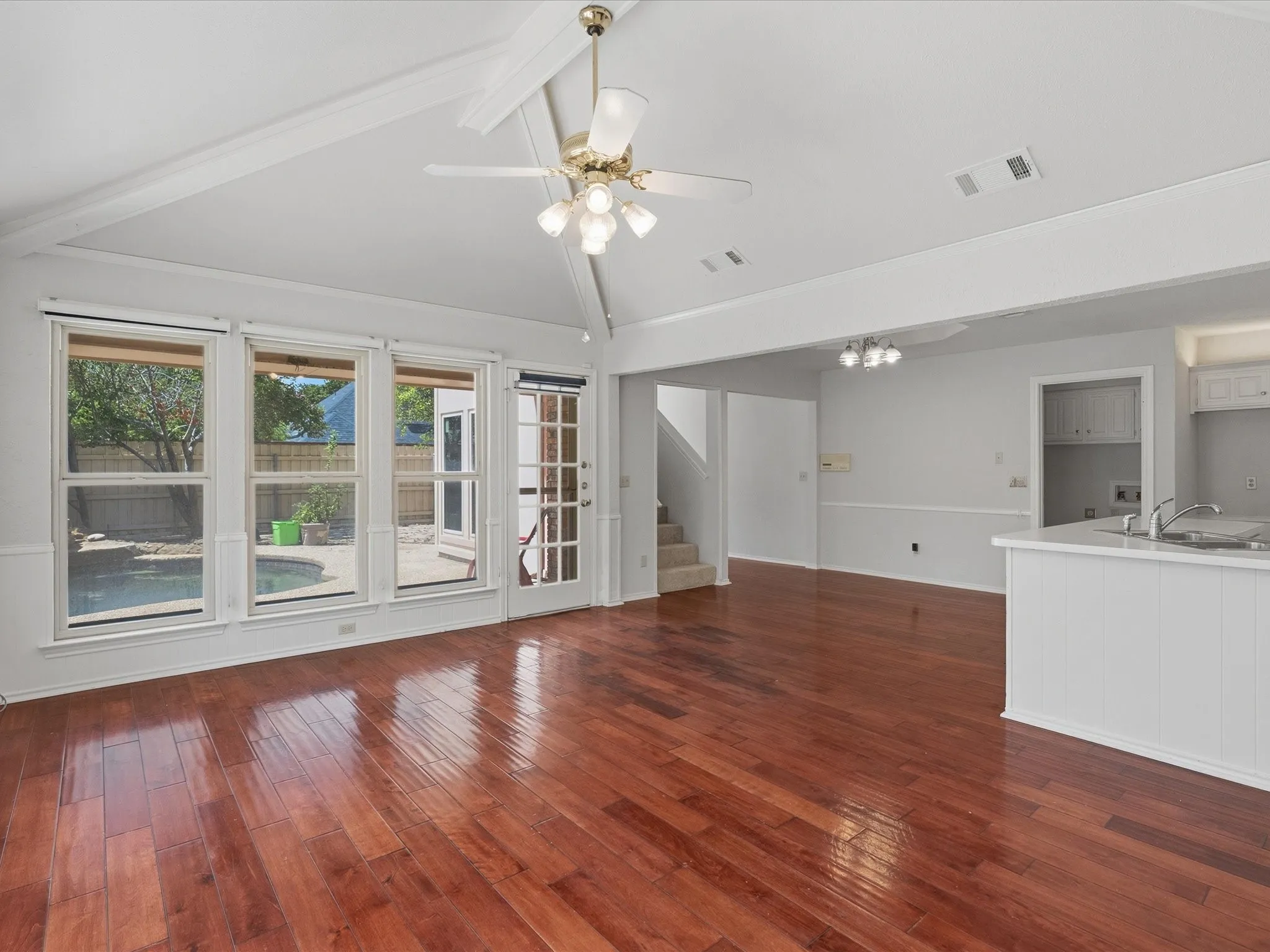 Living area featuring wood-finish flooring, a vaulted ceiling with exposed beams, and a ceiling fan