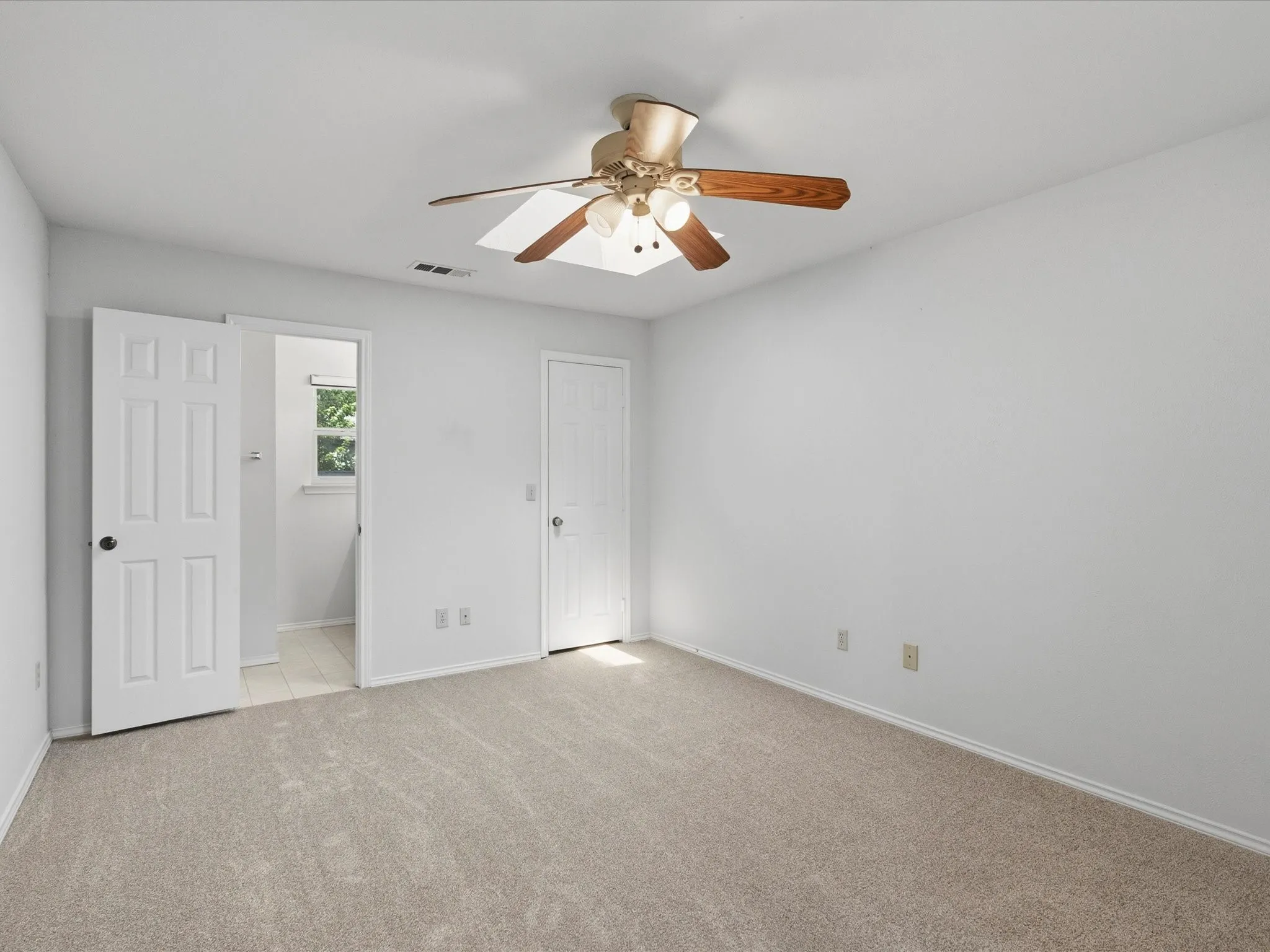 Spacious room featuring neutral carpet flooring, white walls, and a ceiling fan with light fixture