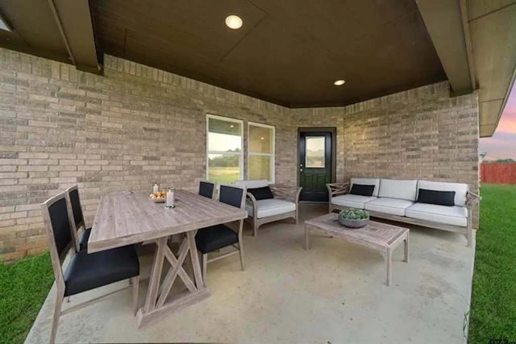 Expansive covered patio featuring a concrete surface, brick exterior wall, and integrated ceiling lighting. Virtually staged.