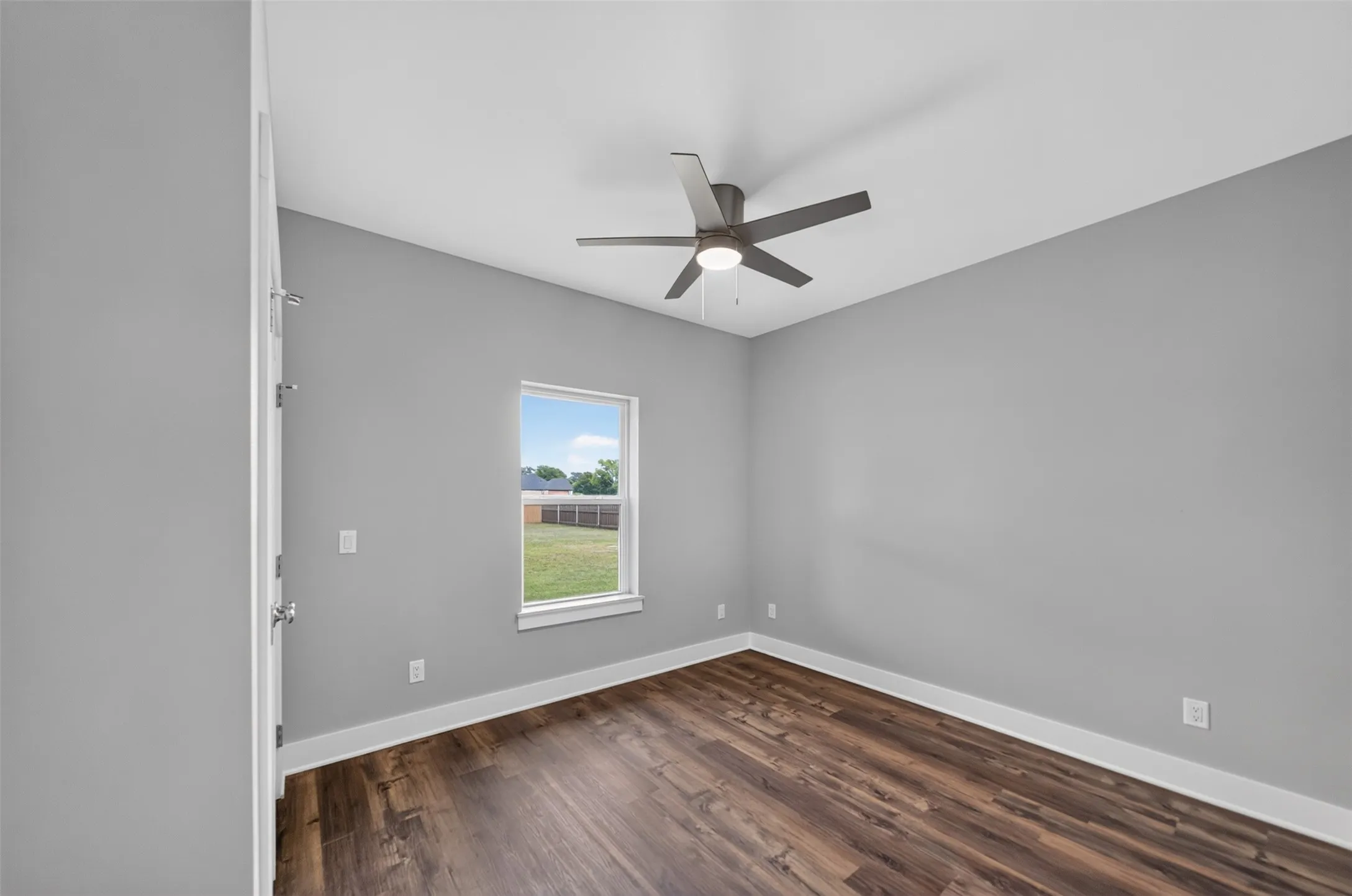 Spacious interior room featuring wood-finish flooring, a contemporary ceiling fan with integrated lighting, and a single window with a white frame